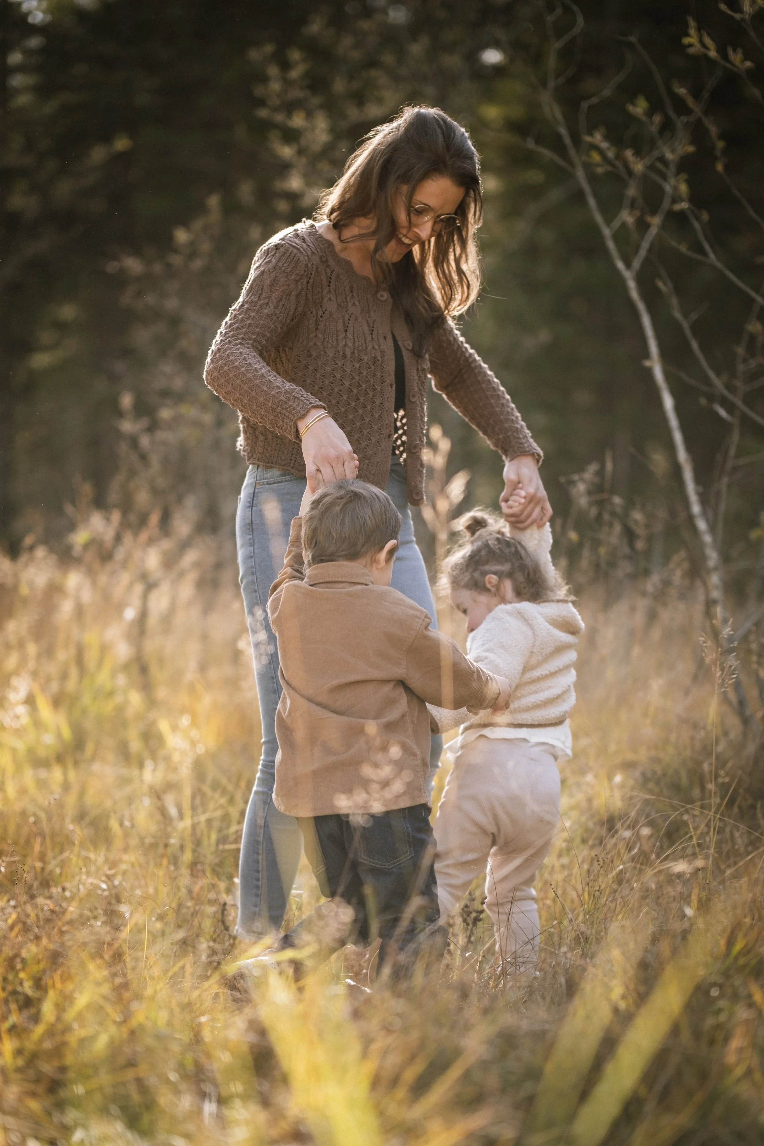 Eine Frau mit zwei Kindern im Freien im Herbst, die sich in einem Feld mit hohem Grase befindet, die Familie hält sich an den Händen.