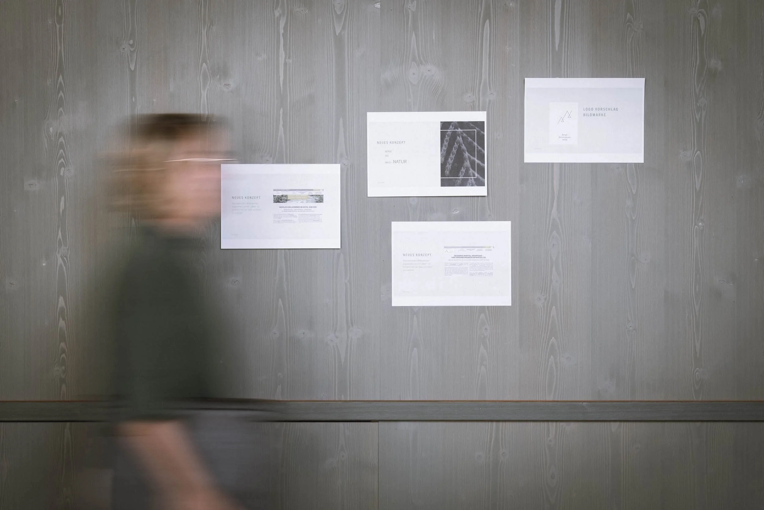 Eine person läuft an einer Wand mit mehreren an Pinnwänden befestigten Papieren vorbei, die Diagramme und Texte enthalten.