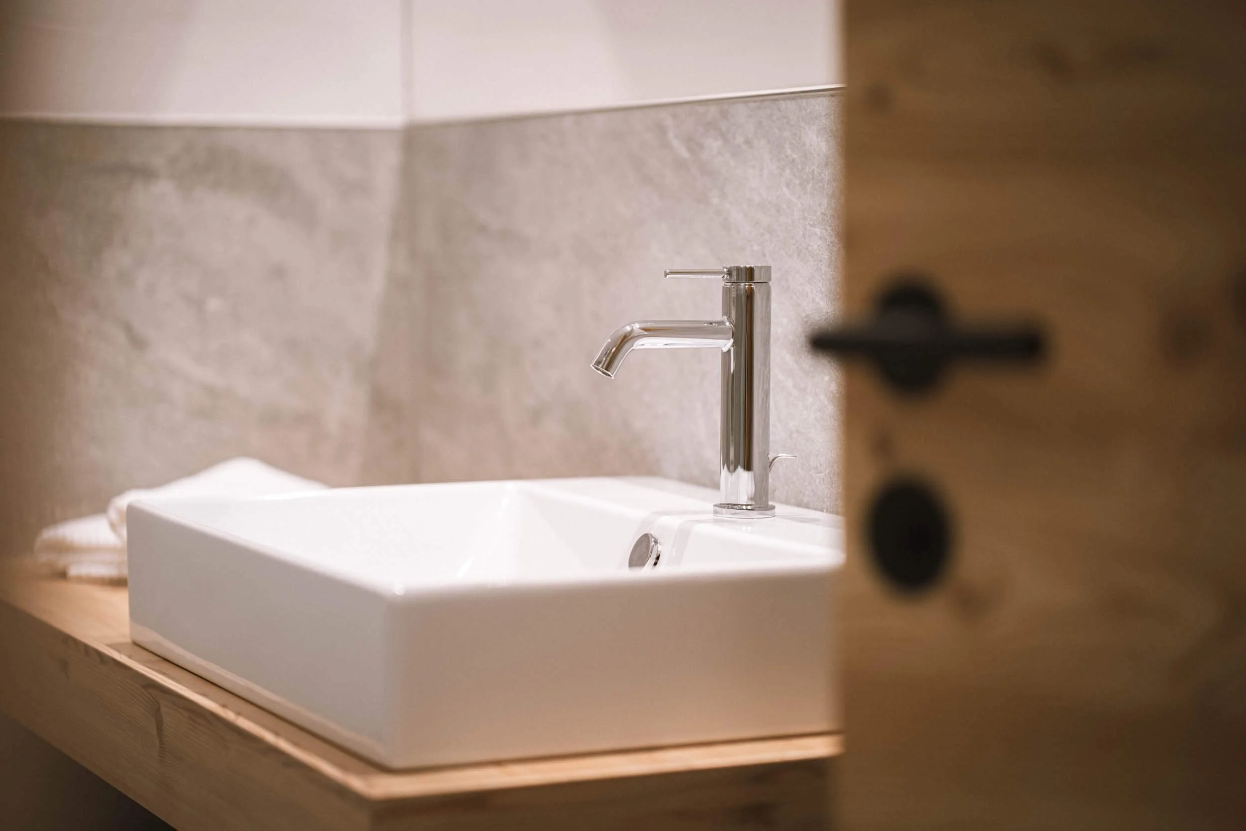 Waschbecken mit Silberarmatur in einem Badezimmer, sichtbar hinter einer halb geöffneten Holztür.