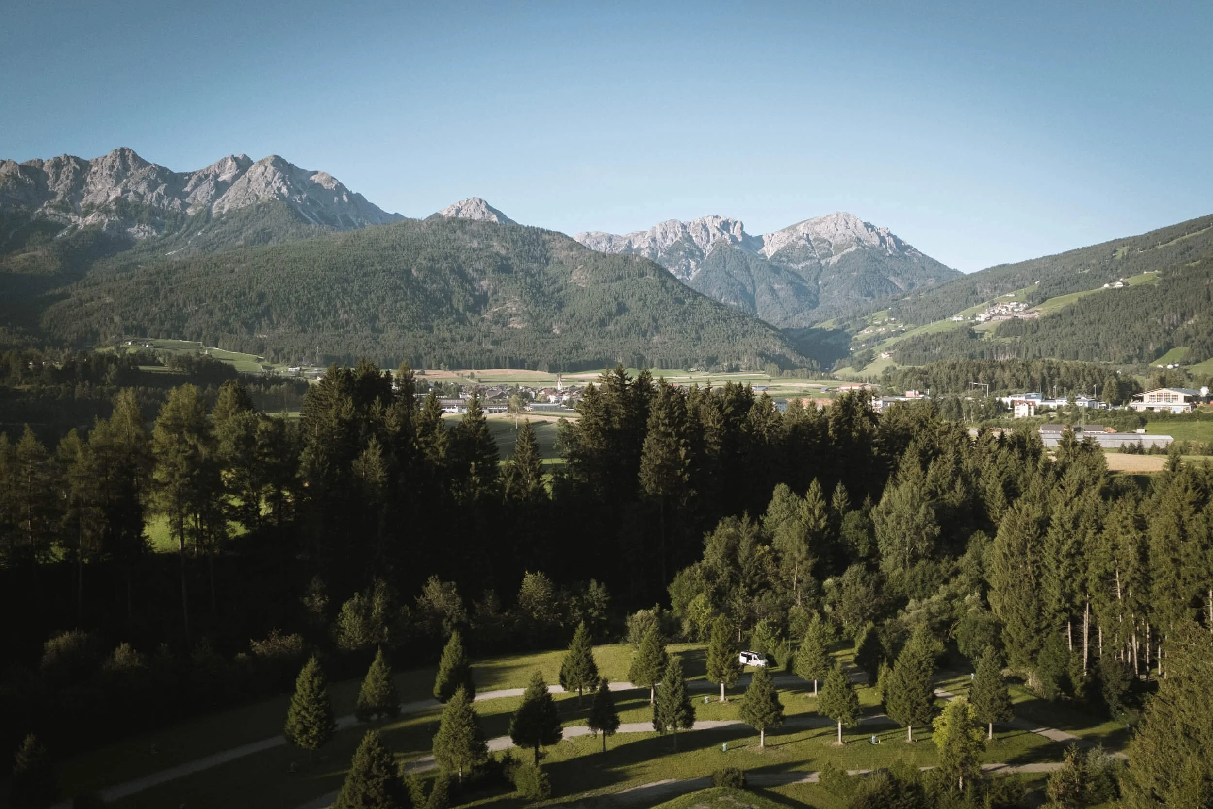 Landschaft mit Bergen im Hintergrund, Wäldern und einer kleinen Ortschaft im Tal bei sonnigem Wetter.