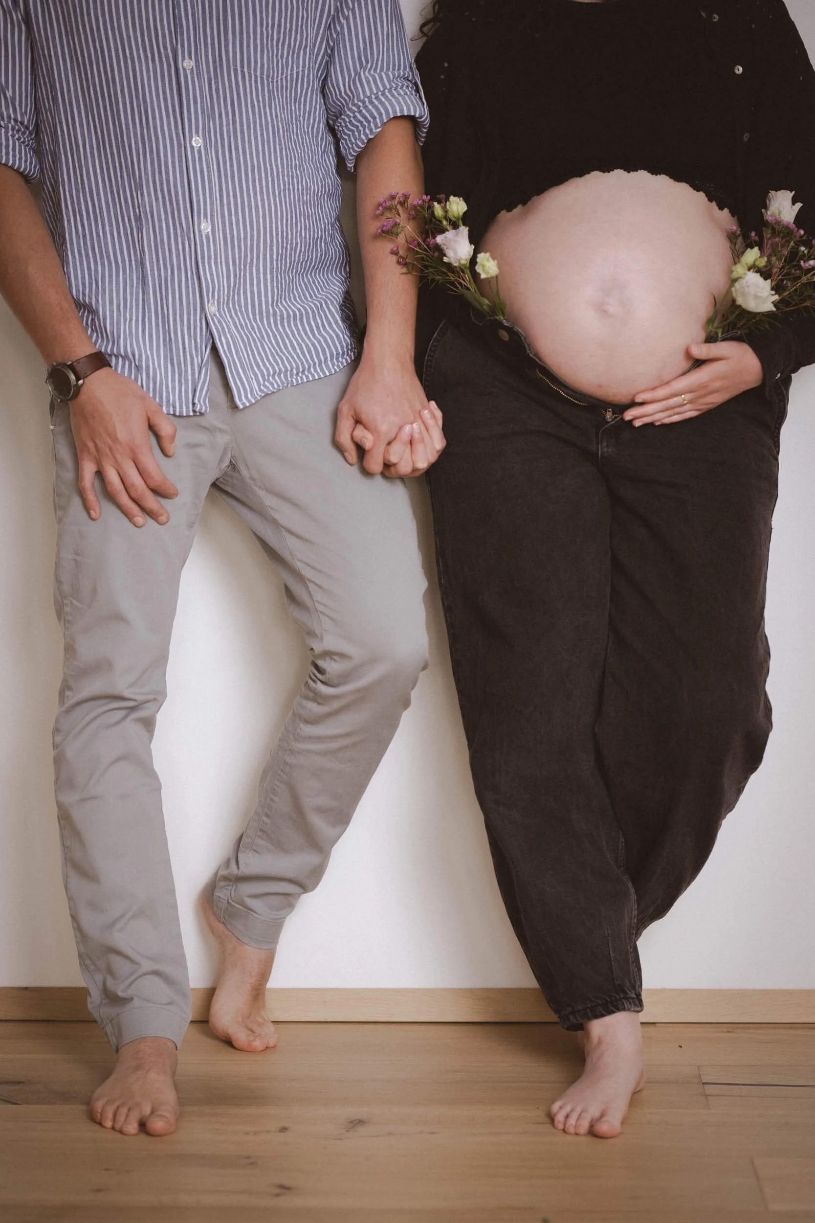 Ein Paar hält sich an den Händen, neben einer schwangeren Frau, die Blumen um den Bauch trägt.