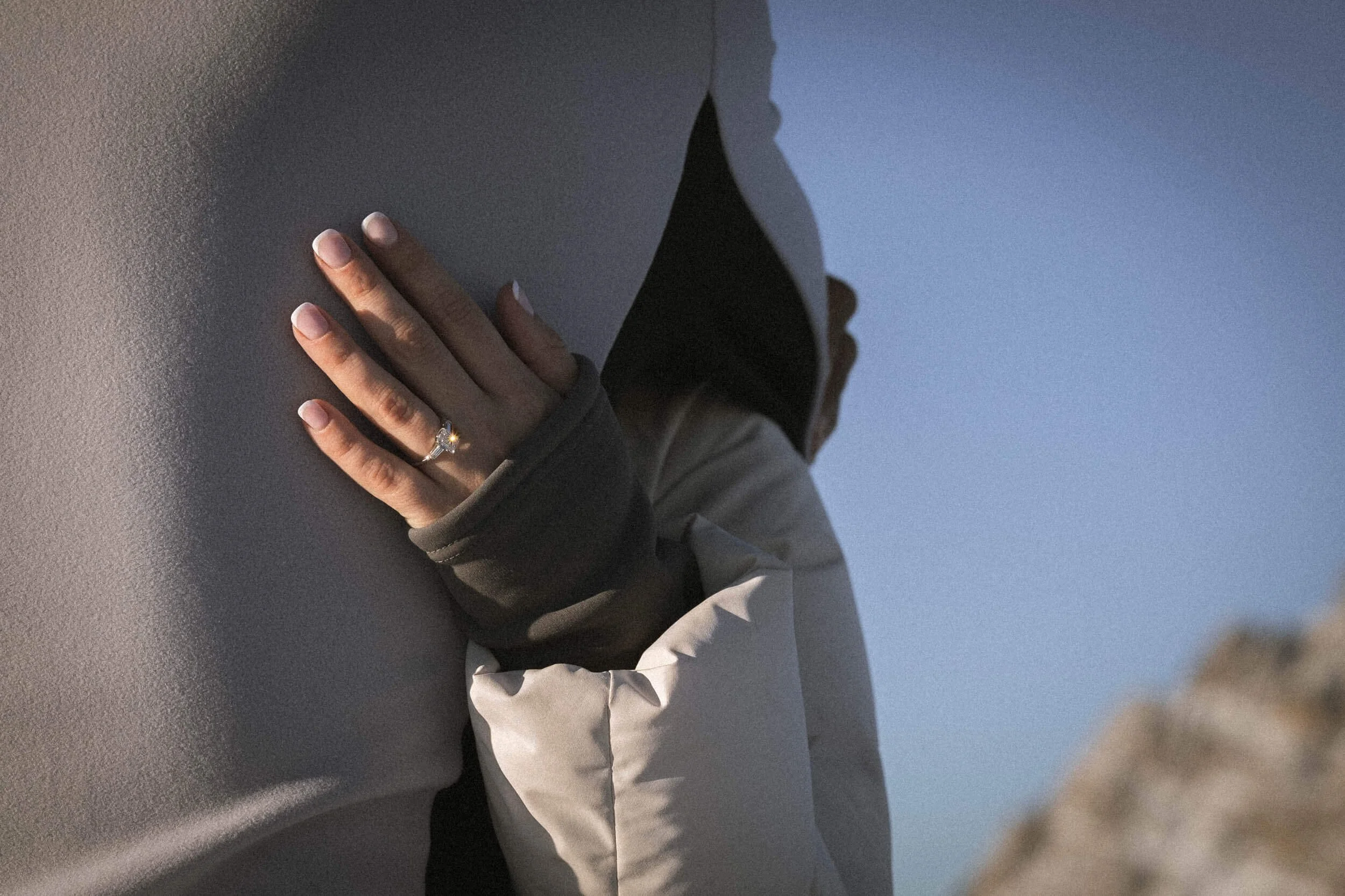 Nahaufnahme einer Hand mit einem Verlobungsring, die gegen eine Wand drückt, bei Sonnenuntergang oder Dämmerung.