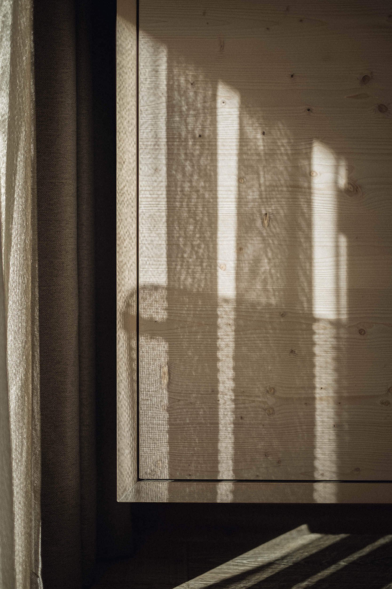 Schatten eines Lamellenvorhangs auf einer Holzoberfläche bei Sonnenlicht.