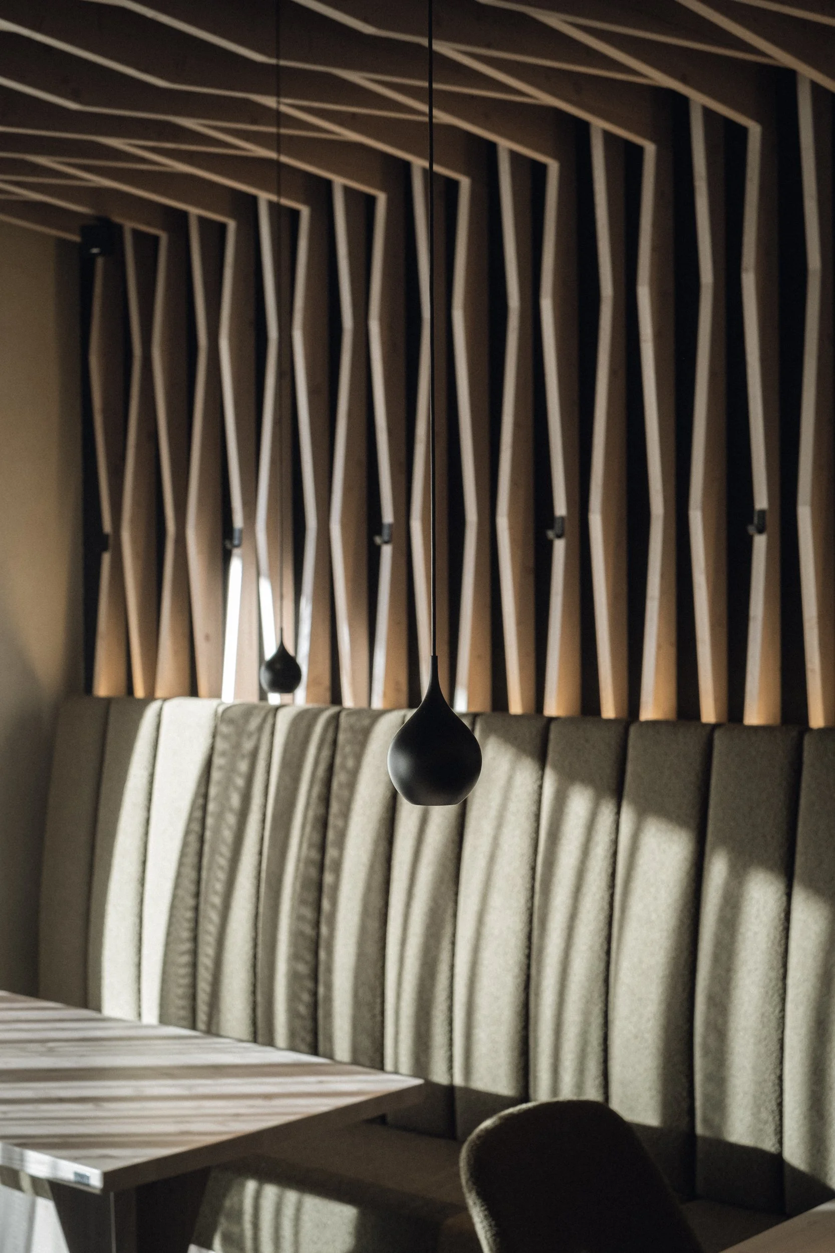 Eleganter Innenraum mit Holzdekor, gepolsterten Sitzbänken und hängenden schwarzen Lampen.