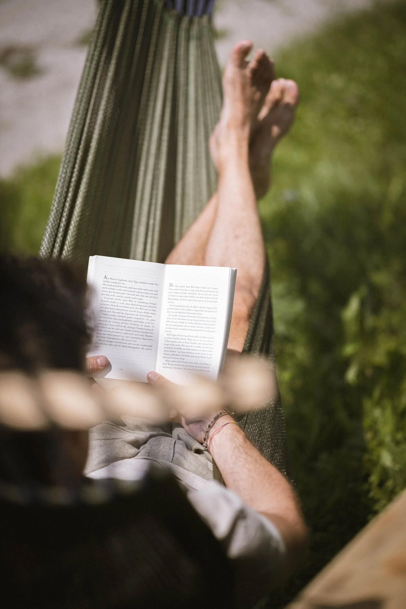 Eine Person liegt in einer Hängematte im Freien und liest ein Buch.