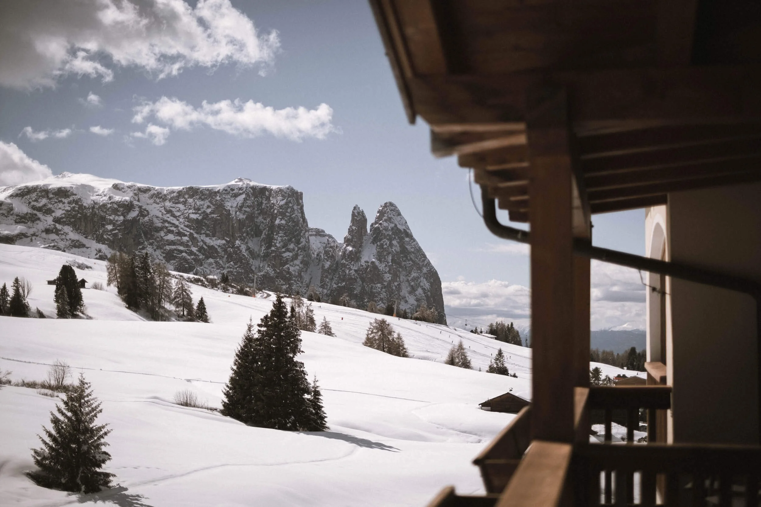 Schneebedeckte Berge und Tannenbäume auf einer Winterlandschaft, gesehen von einem Balkon eines Hauses in den Alpen, bei sonnigem Himmel.