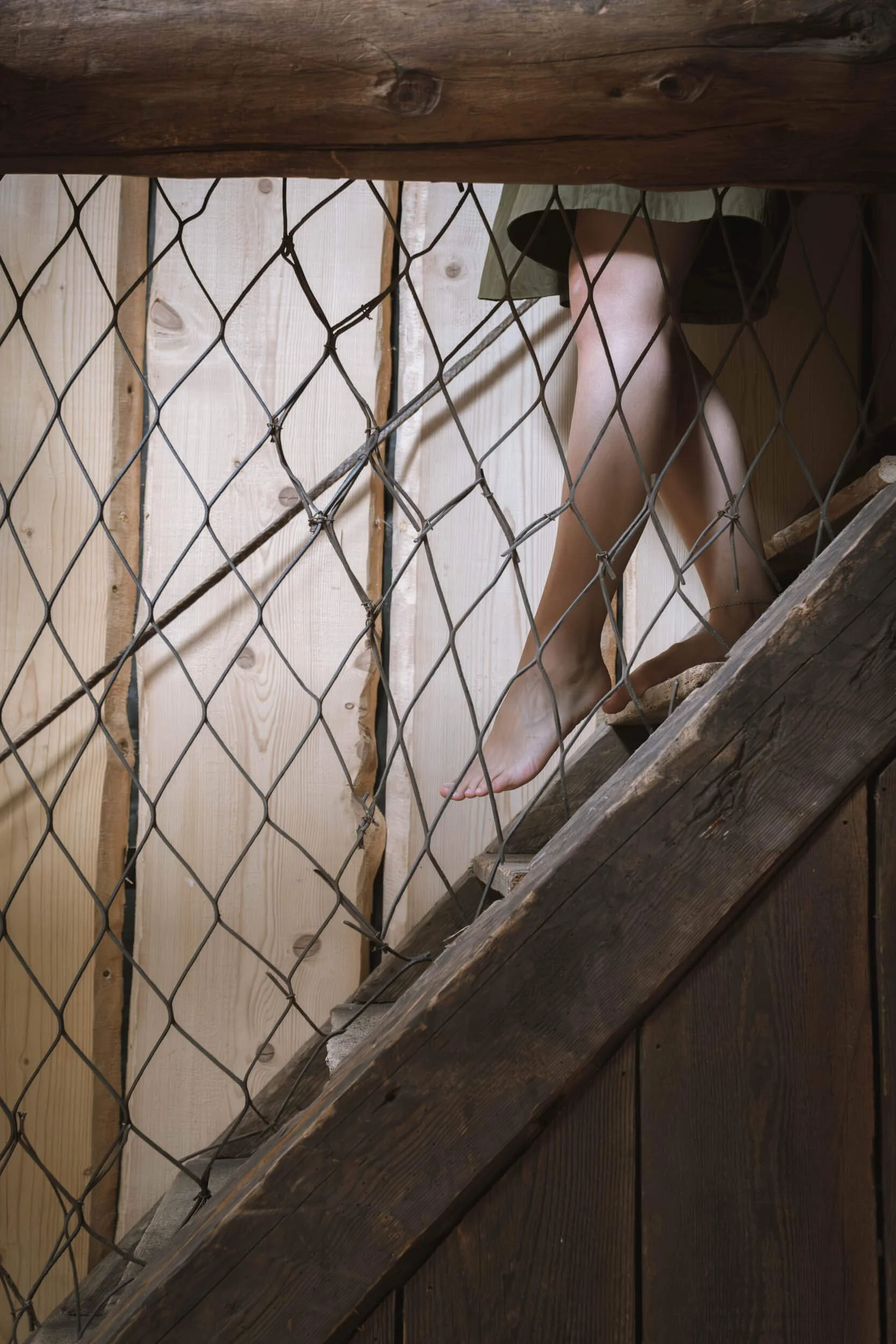Eine Person steigt eine Treppe aus Holz in einem Raum mit Holzwänden, Sicht durch einen Drahtzaun.