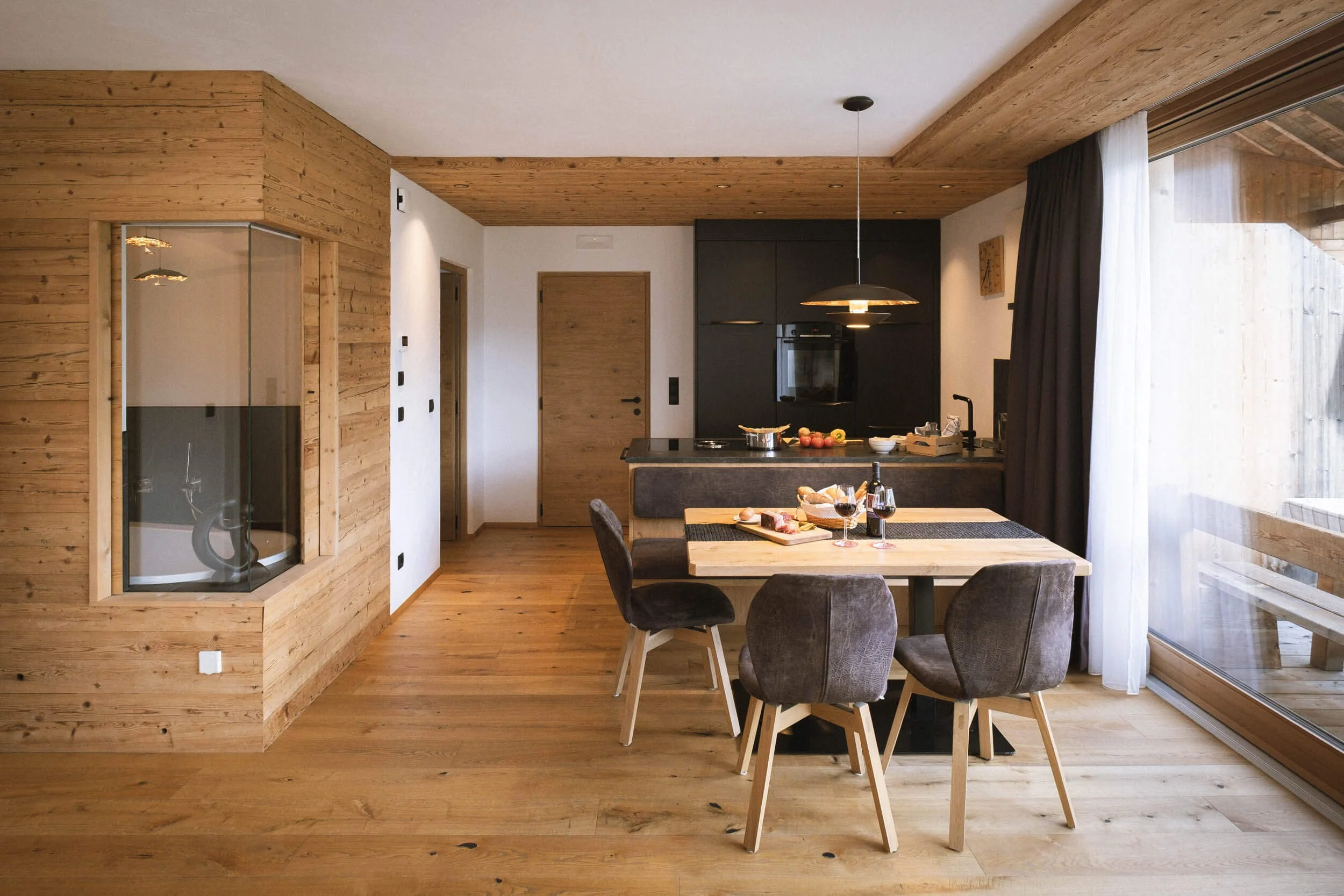 Moderne, offene Wohnküche mit Holzdecke, Esstisch mit fünf Stühlen, zum Essen gedeckt, große Fenster mit Blick auf einen Balkon oder Terrasse.