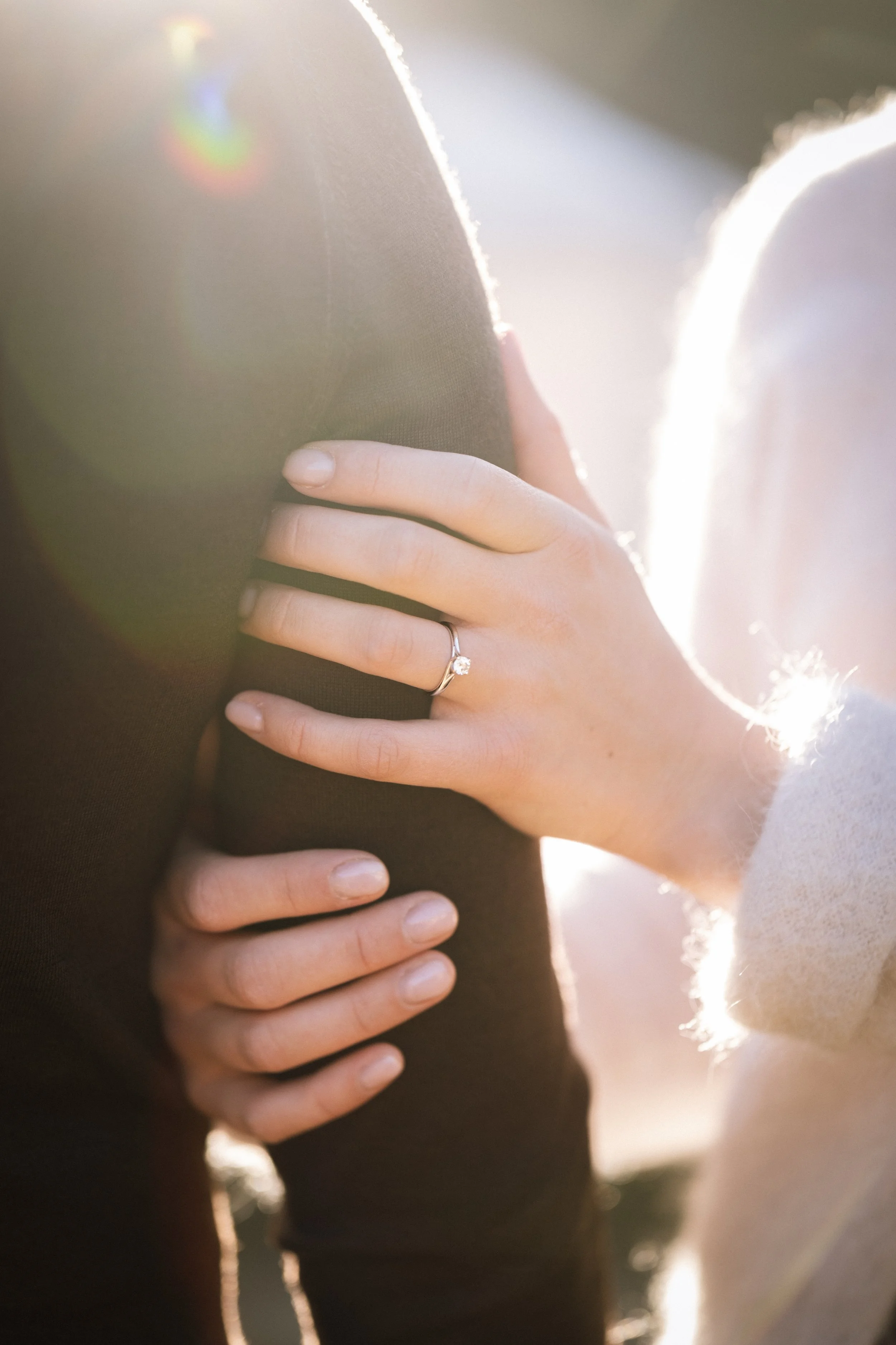 Nahaufnahme eines Rings am Finger einer Frau, die eine Schulter eines Mannes berührt, bei Sonnenlicht im Freien