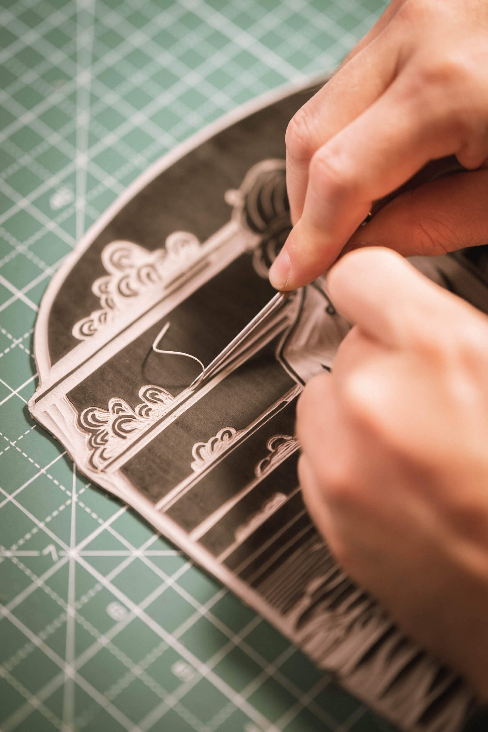 Eine Hand sticht in eine aus Papier geschnittene schwarz-weiße Vorlage, während sie auf einem Schneideuntergrund liegt.