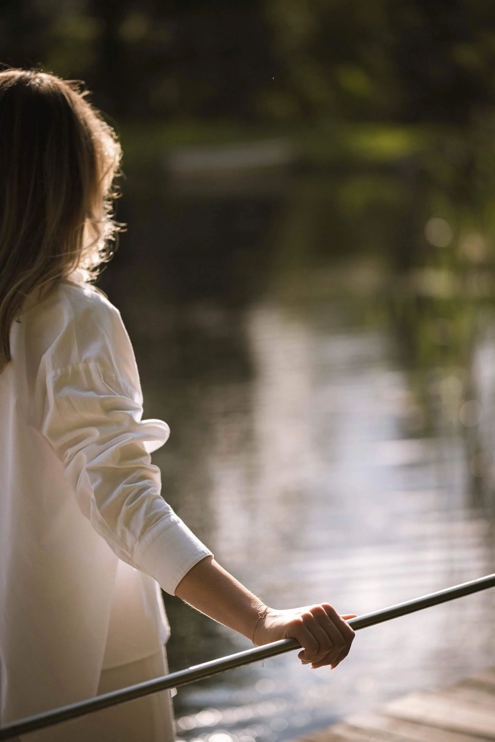 Junge Frau steht am Wasser und hält eine Stange, Blick auf den Fluss bei Sonnenuntergang, entspannte Stimmung, Natur