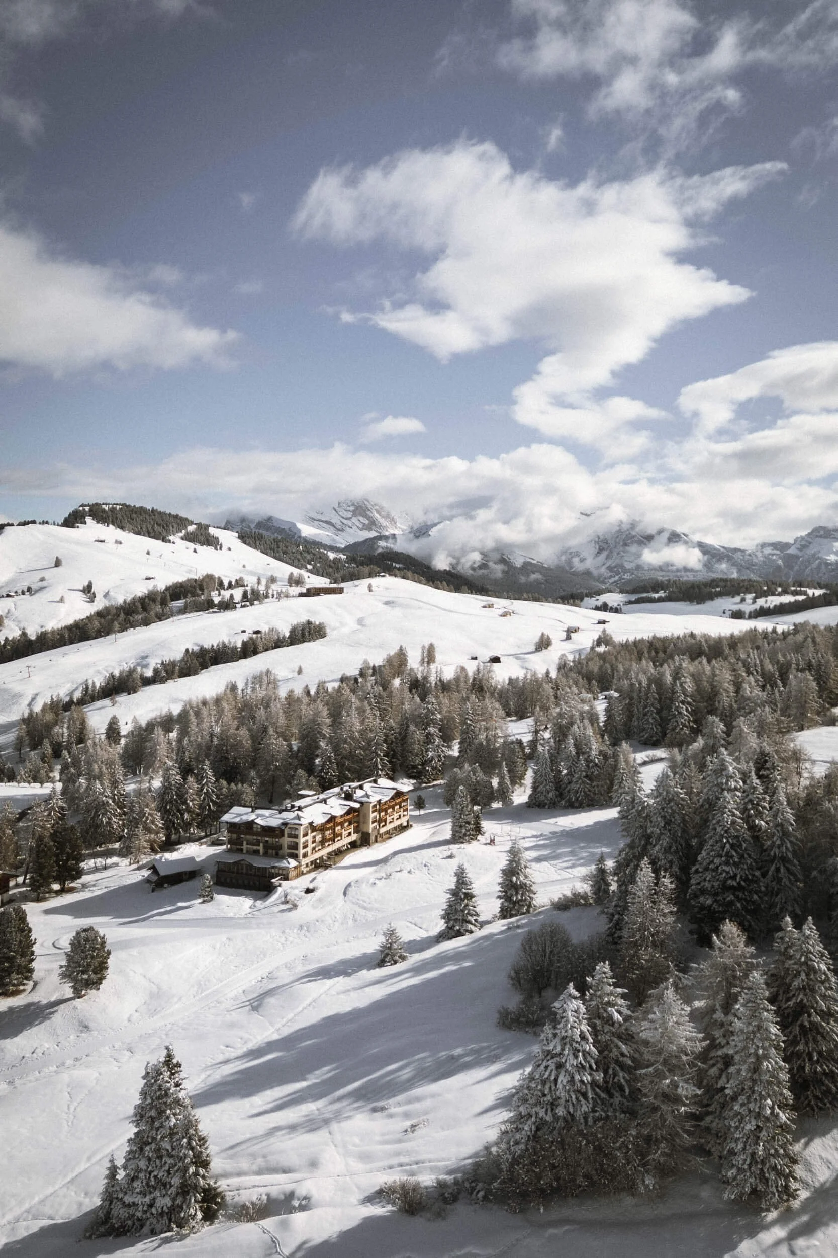 Schneebedeuerte Berge und Tannen in einer Winterlandschaft mit einem großen Hotel im Vordergrund.