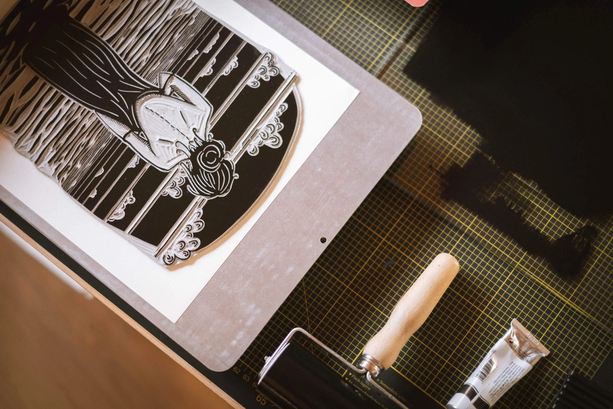 Linolschnitt mit einem George Washington Porträt, eine Schneidwalze, ein Messer und Druckfarben auf einer Arbeitsfläche.