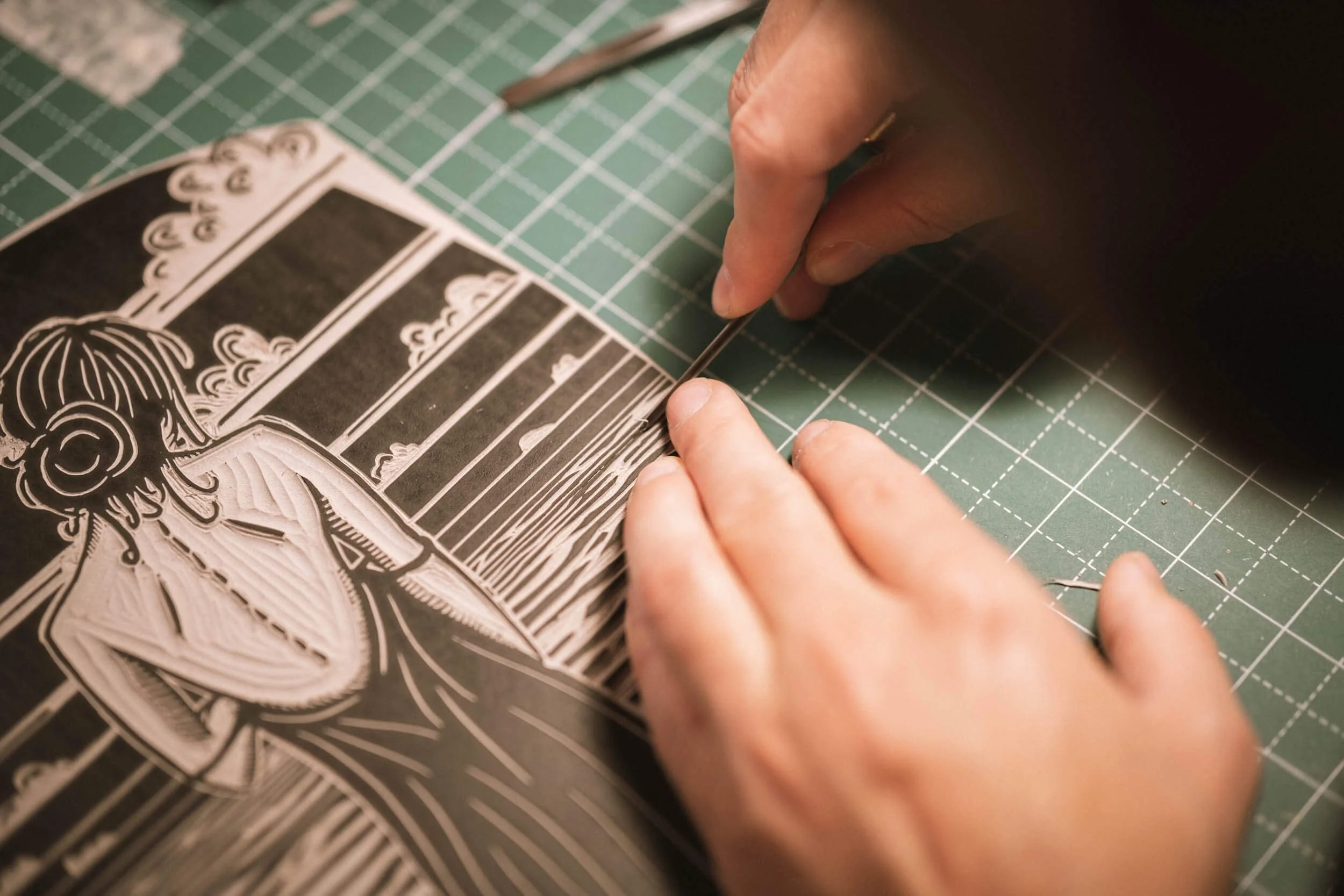 Nahaufnahme einer Person, die eine Linolschnittdruckplatte mit einem Werkzeug bearbeitet, auf einem grünen Schneidebrett.