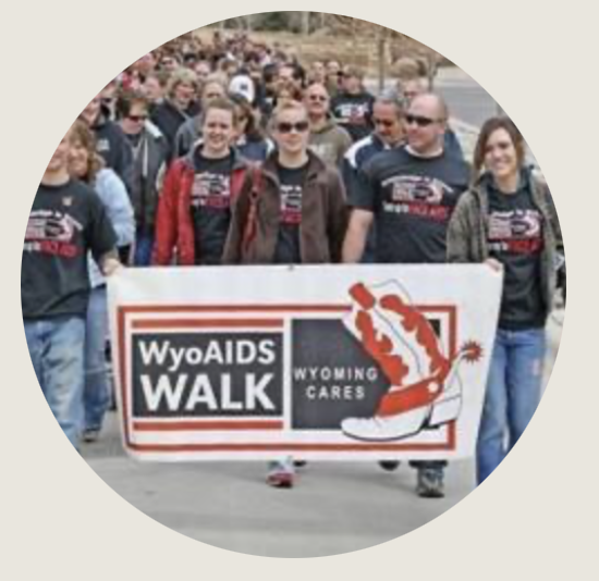 Group of people standing behind a banner that says, WyoAIDS WALK, Wyoming Cares with a red and white cowboy boot