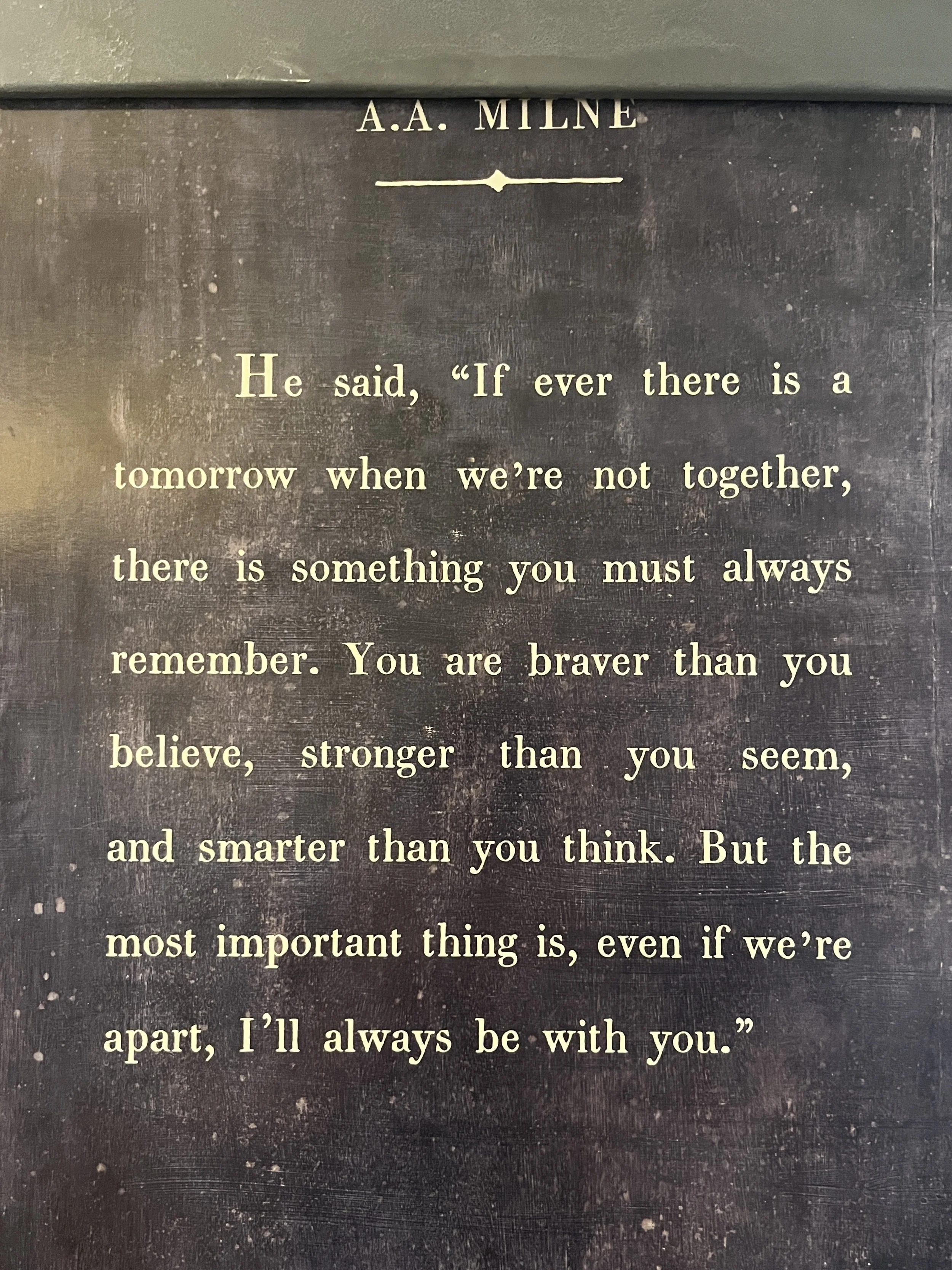 Weathered dark sign displaying an A.A. Milne quotation about courage, strength, and staying connected.