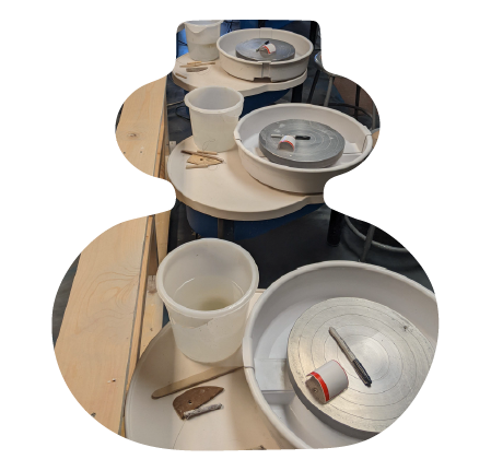 Pottery wheel stations with clay, tools, and cups in a pottery studio