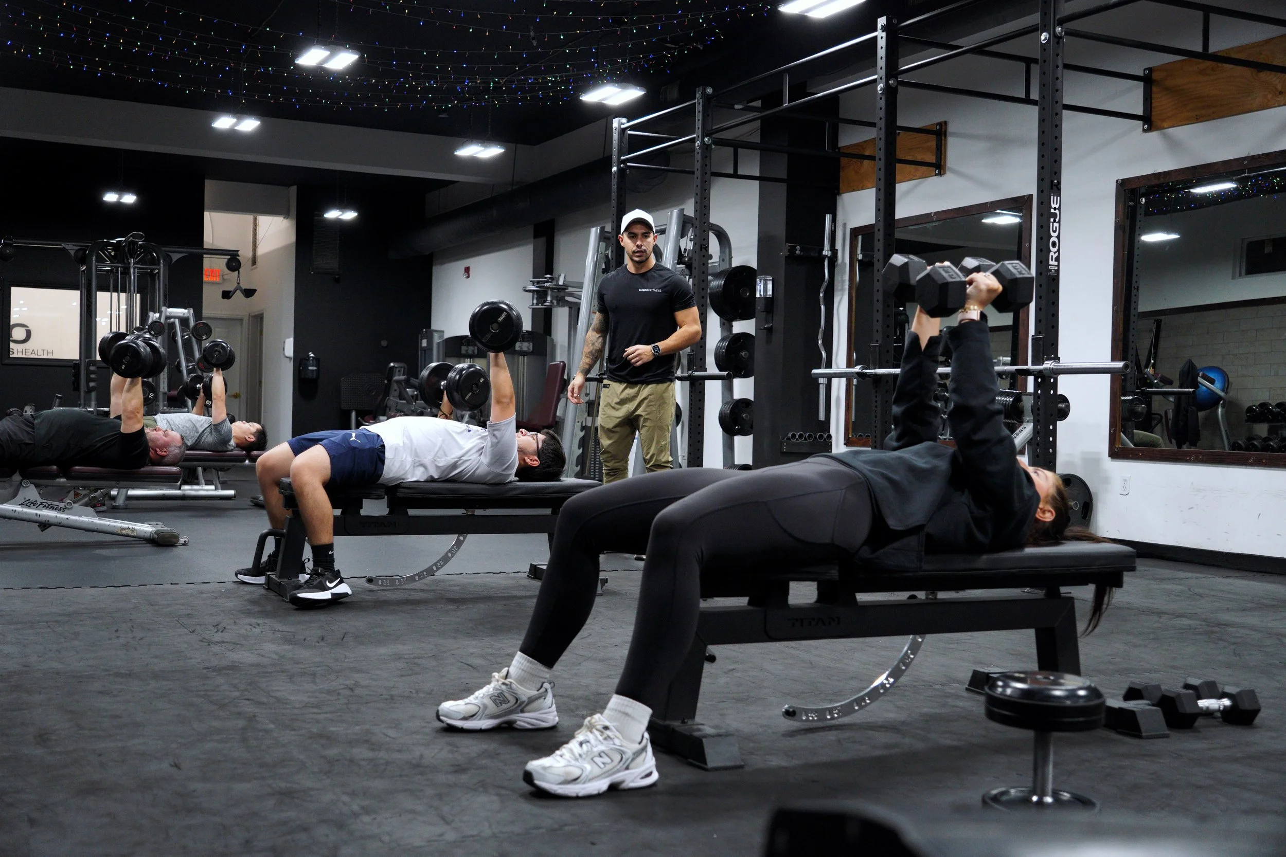 Members performing dumbbell bench presses during a structured semi-private training session at EMBODI Fitness, coached and monitored for proper form.