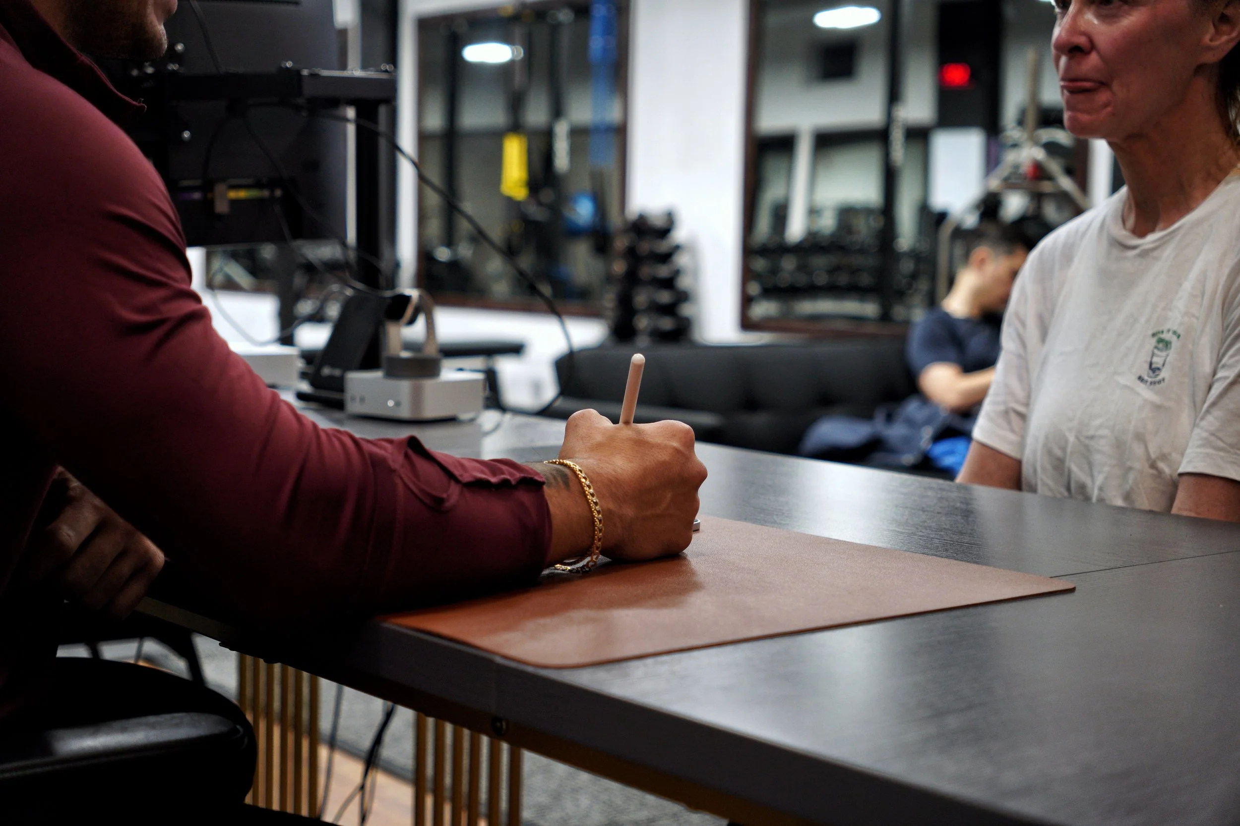 Coach writing on a tablet during a fitness consultation with a client at EMBODI Fitness, seated across a desk in the studio lobby.