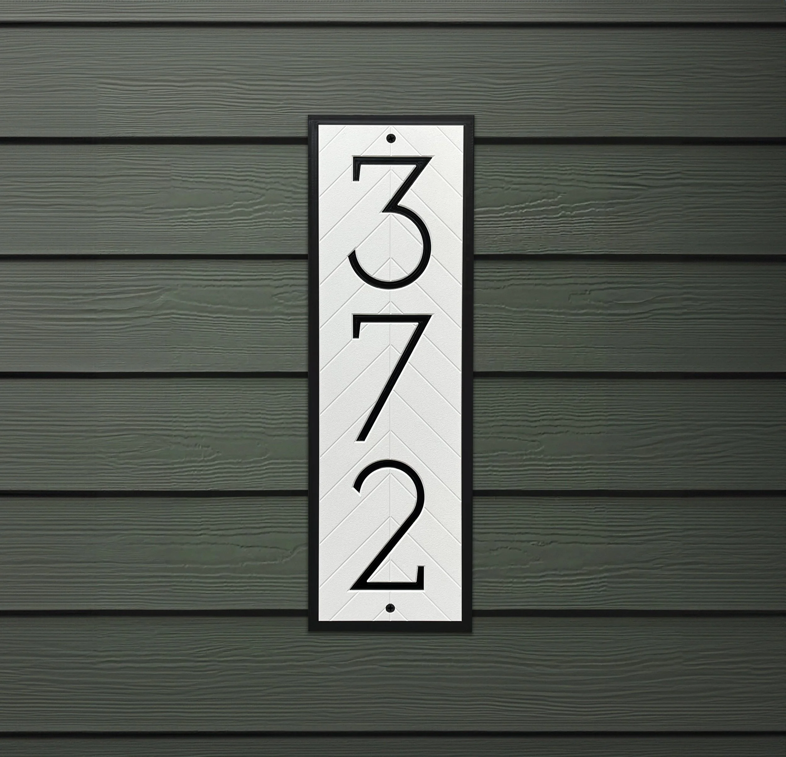 Vertical herringbone house number sign displaying 372 mounted on dark green lap siding — white HDPE address plaque with black border showing three-digit configuration, made to order in the USA