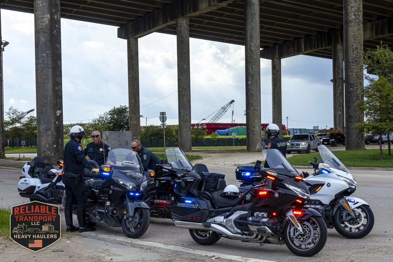 Police motorcycle escort officers with their bikes lined up under an elevated highway, ready to escort a wide load convoy