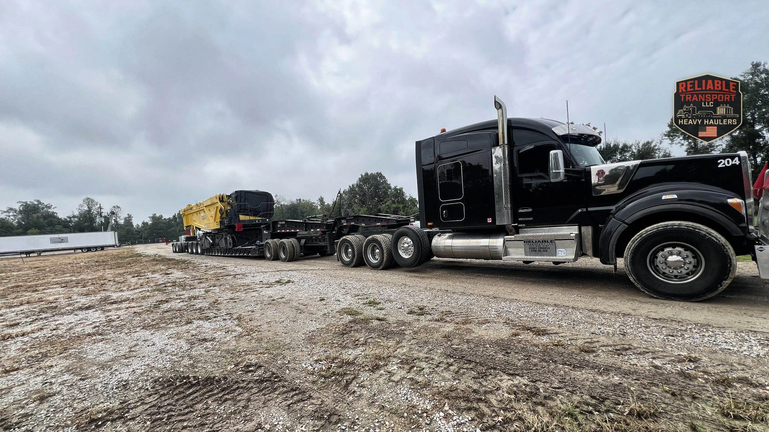 Black heavy haul tractor pulling yellow and black crane components on a multi axle trailer across a gravel lot
