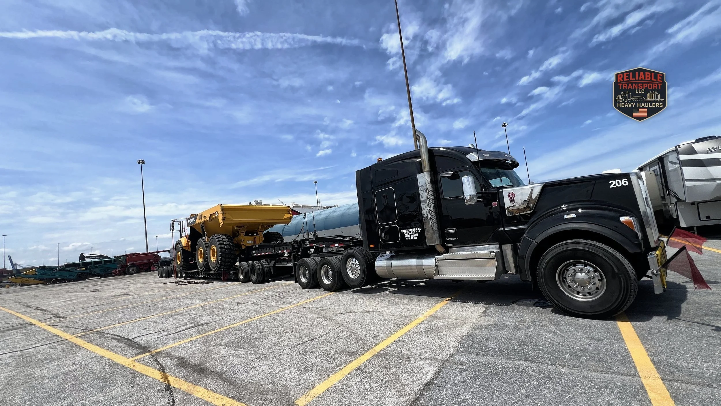Black heavy haul tractor pulling a yellow articulated dump truck on a multi axle trailer across a wide paved lot
