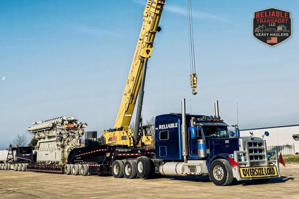 Blue truck unit 202 with an OVERSIZE LOAD sign, the 220,000 lb submarine engine loaded behind it and a yellow crane beside it