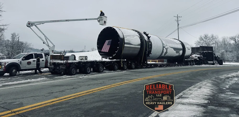 Bucket truck crew lifting overhead lines as the 207,000 lb dryer drum rolls along a snowy road on a heavy haul trailer