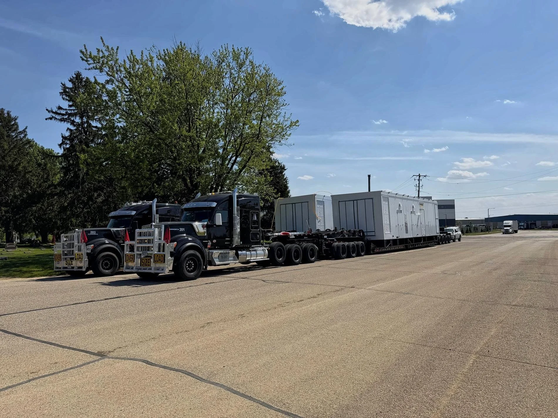 Two black Reliable Transport trucks side by side on a street, with white generator enclosures on a long trailer
