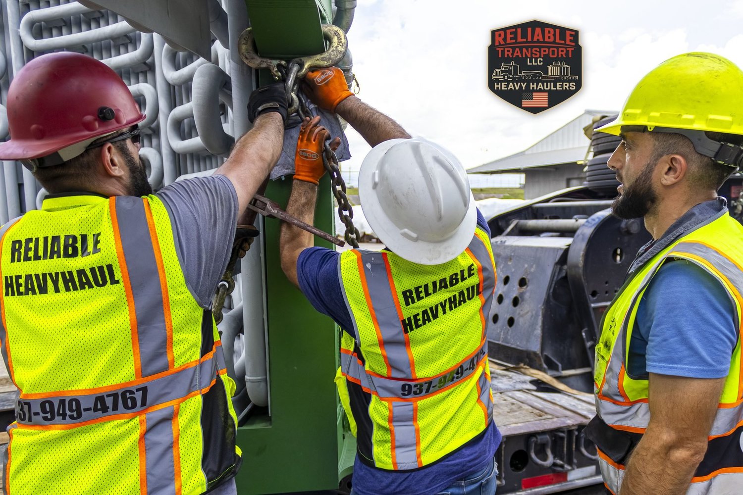 Crew in hard hats and high visibility vests chaining down a wide load on the trailer