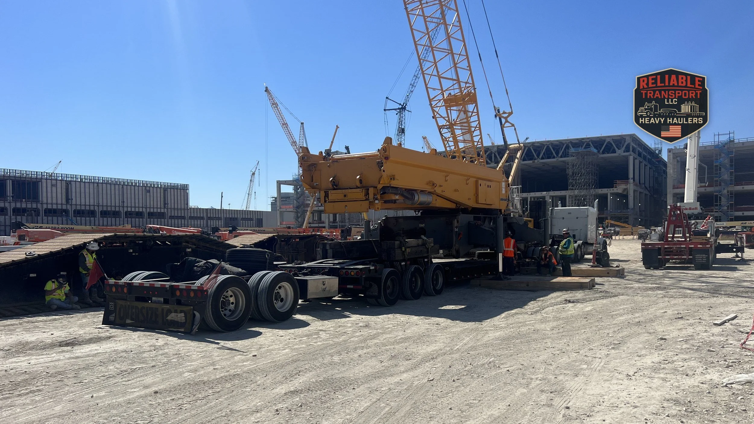 Yellow crane upper section on a multi axle trailer at a busy construction site under a blue sky