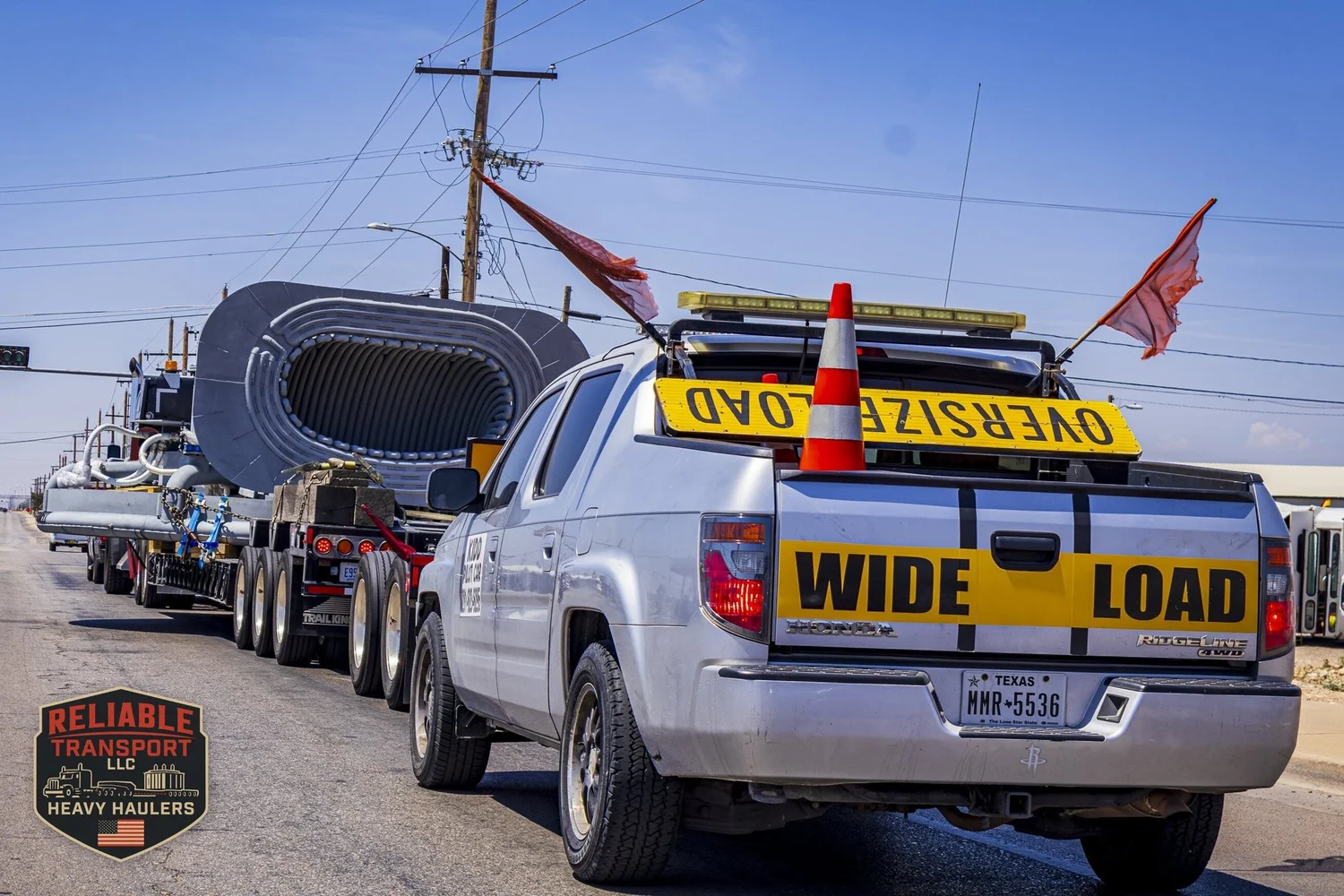 Escort pickup with WIDE LOAD and OVERSIZE LOAD signs and red flags following a wide load down a city street