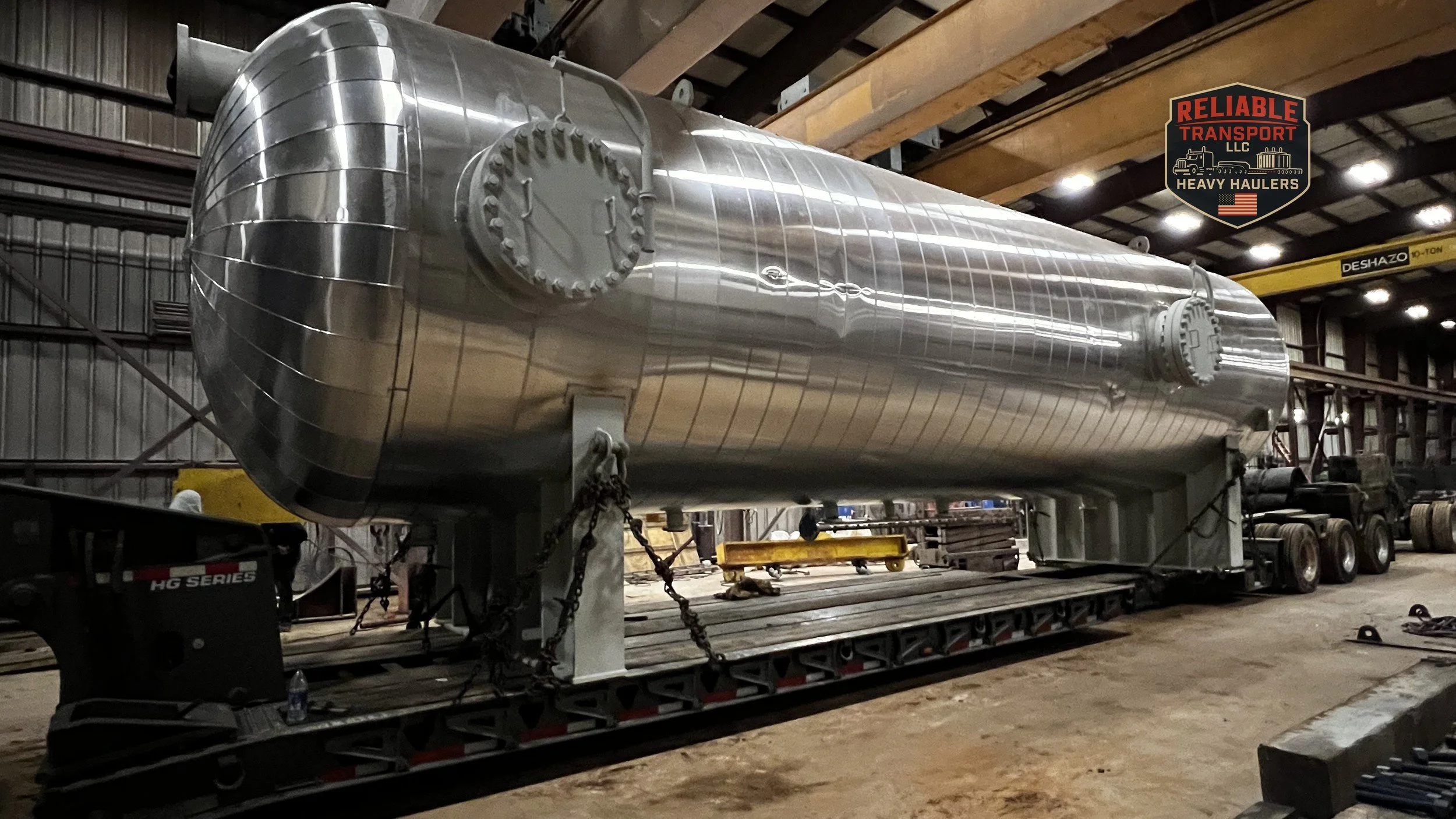Large insulated steel pressure vessel chained to a multi axle trailer inside a fabrication shop