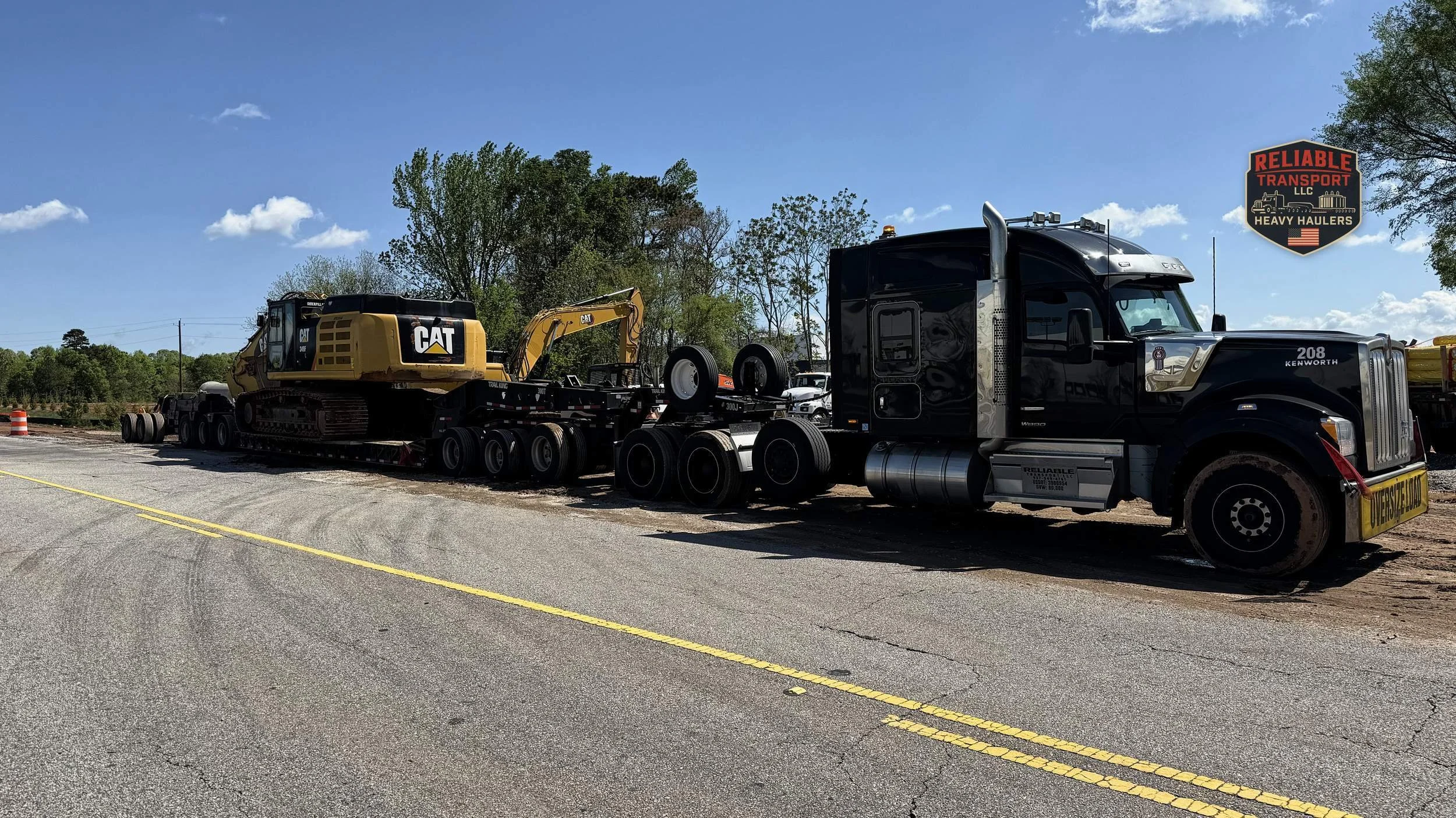 Black heavy haul tractor pulling a yellow excavator on a multi axle trailer under a blue sky