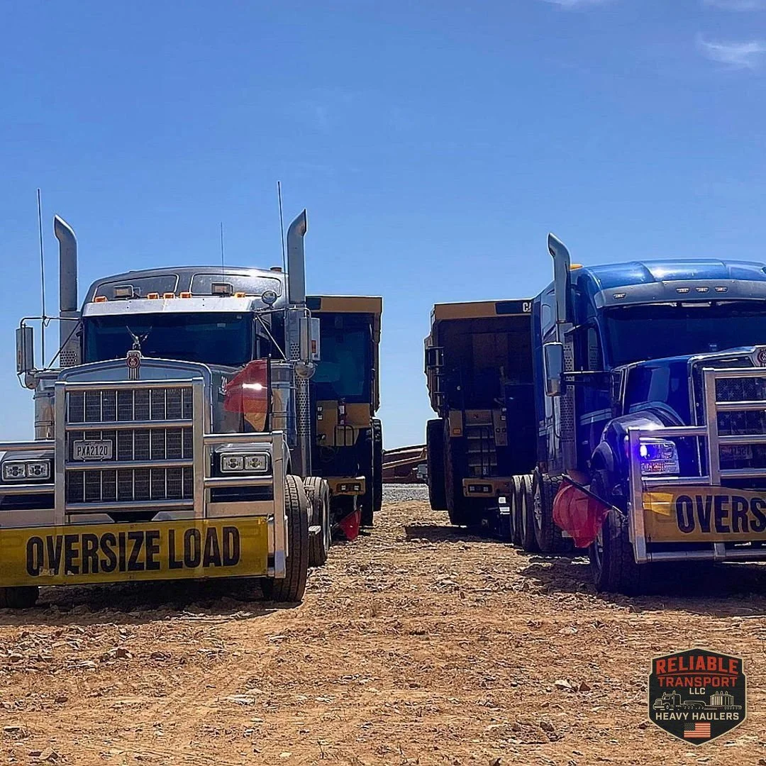Heavy haul trucks with OVERSIZE LOAD banners staged side by side on a dirt lot