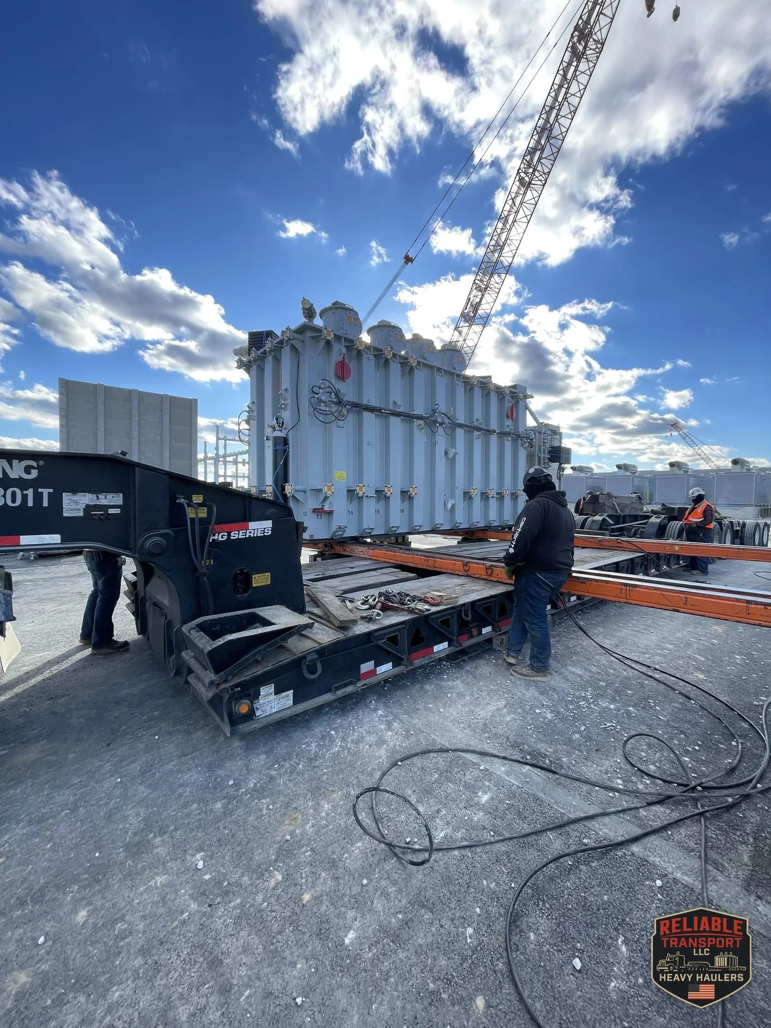 The 160,000 lb transformer on the trailer with orange skid beams alongside and a lattice boom crane behind it, crew working in the foreground