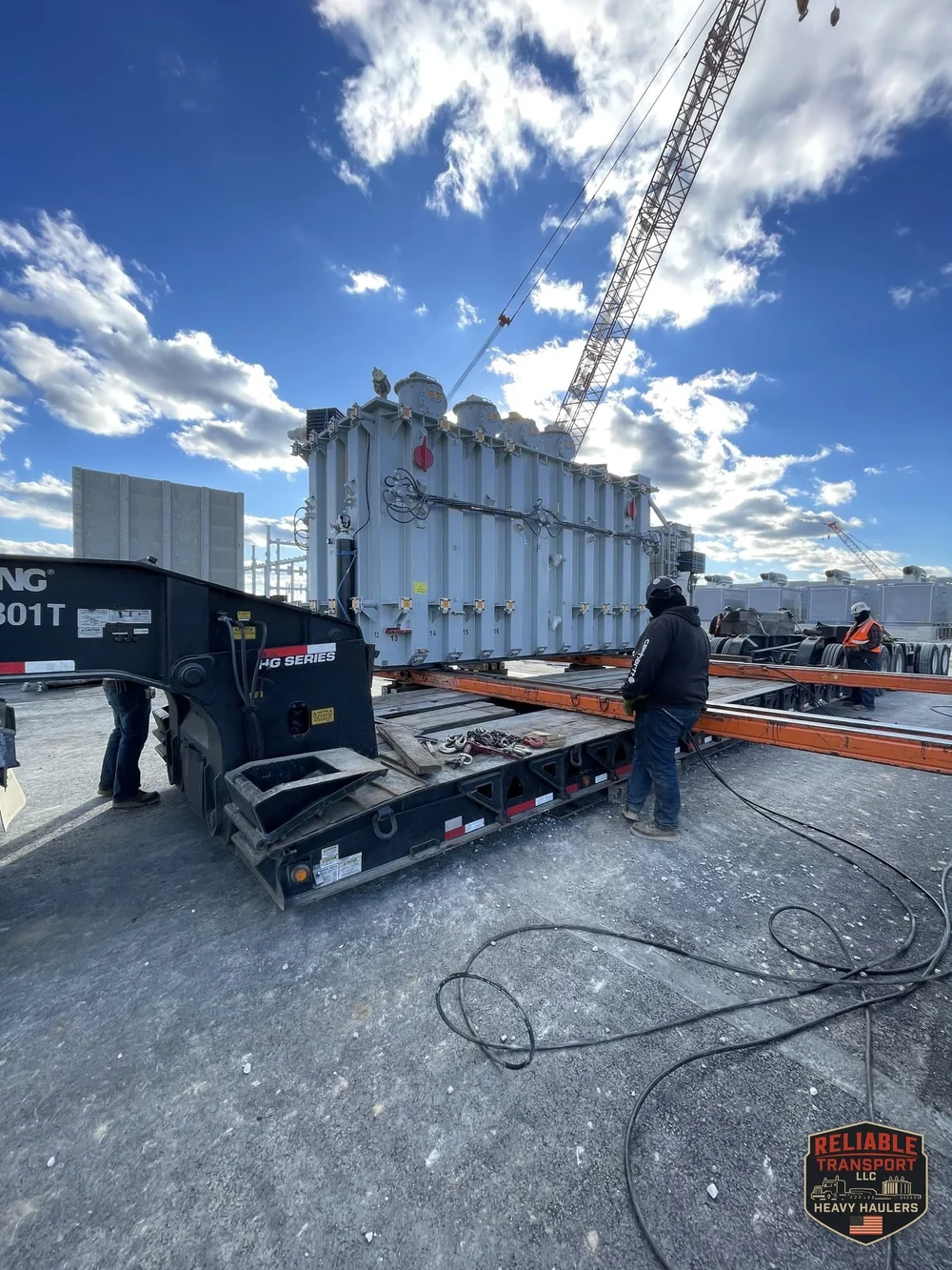 The 160,000 lb transformer on our trailer with orange skid beams alongside and a lattice boom crane behind it at the Obetz site