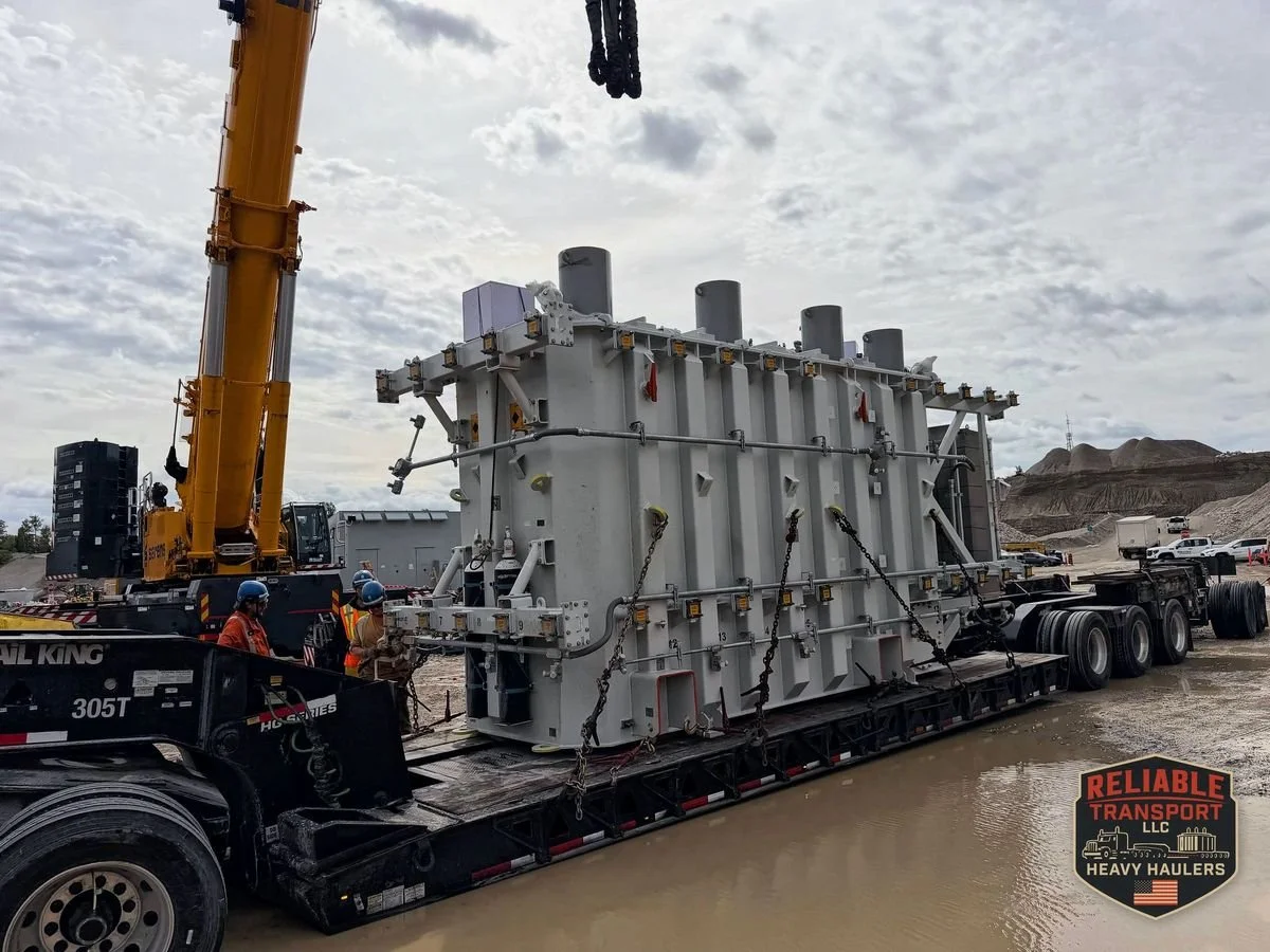 Transformer chained down on a multi axle trailer beside a yellow mobile crane, crew in hard hats and safety vests