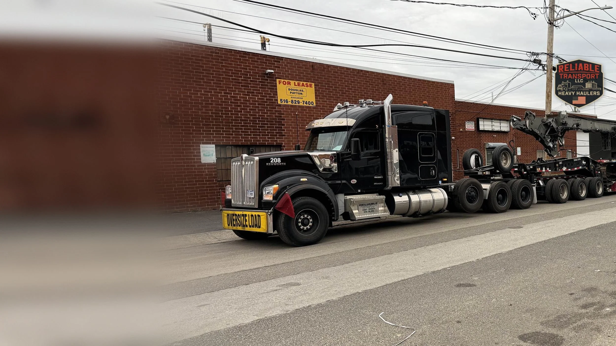Black heavy haul tractor with an oversize load banner pulling a crane on a multi axle trailer along a city street