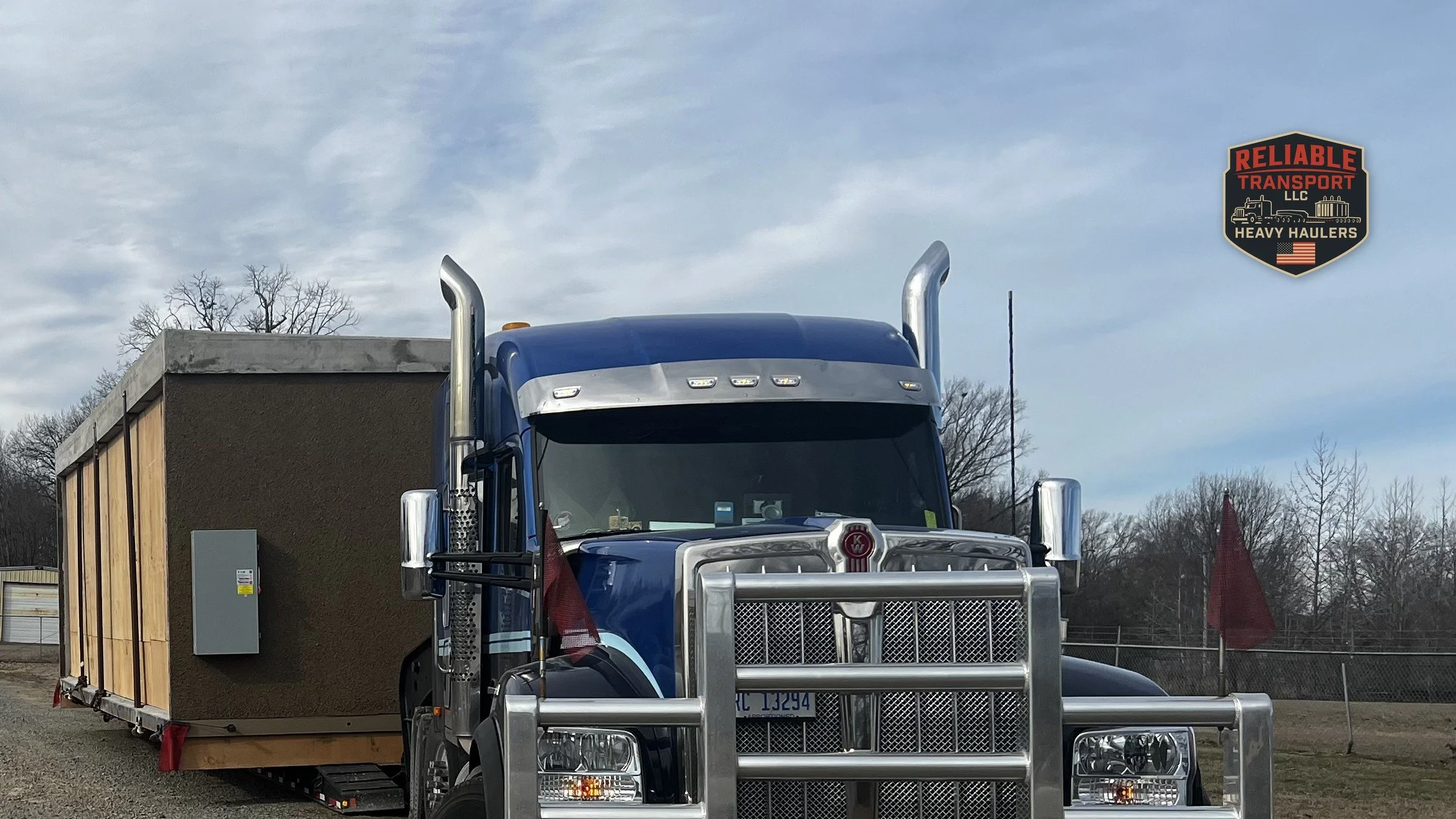 Gray electrical transformer on a multi axle trailer in an open paved yard under a blue sky