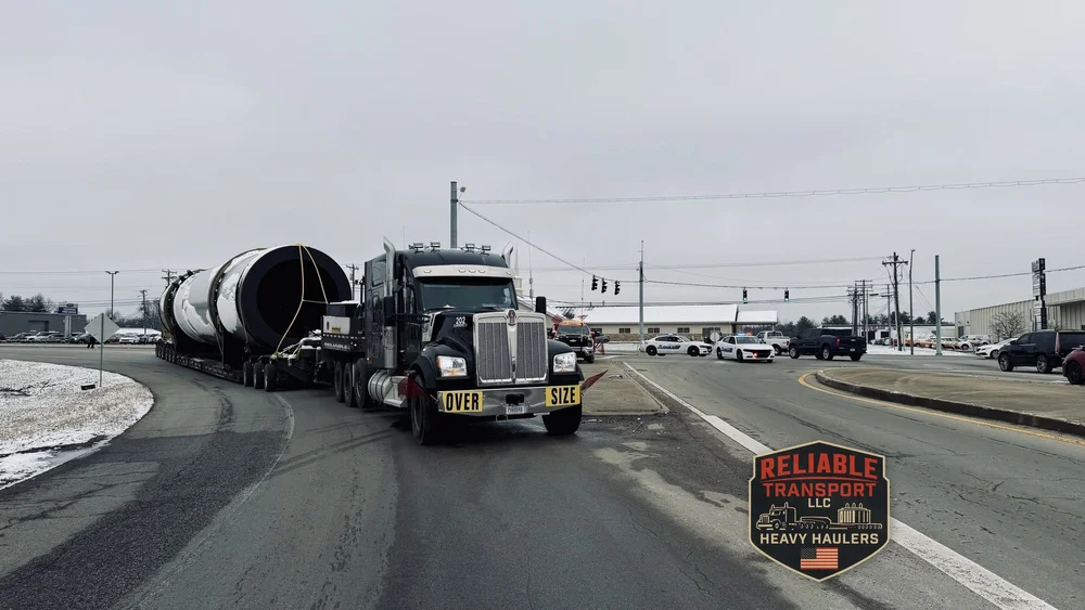 Black heavy haul truck with an OVERSIZE banner pulling the dryer drum through an intersection while police cars hold traffic