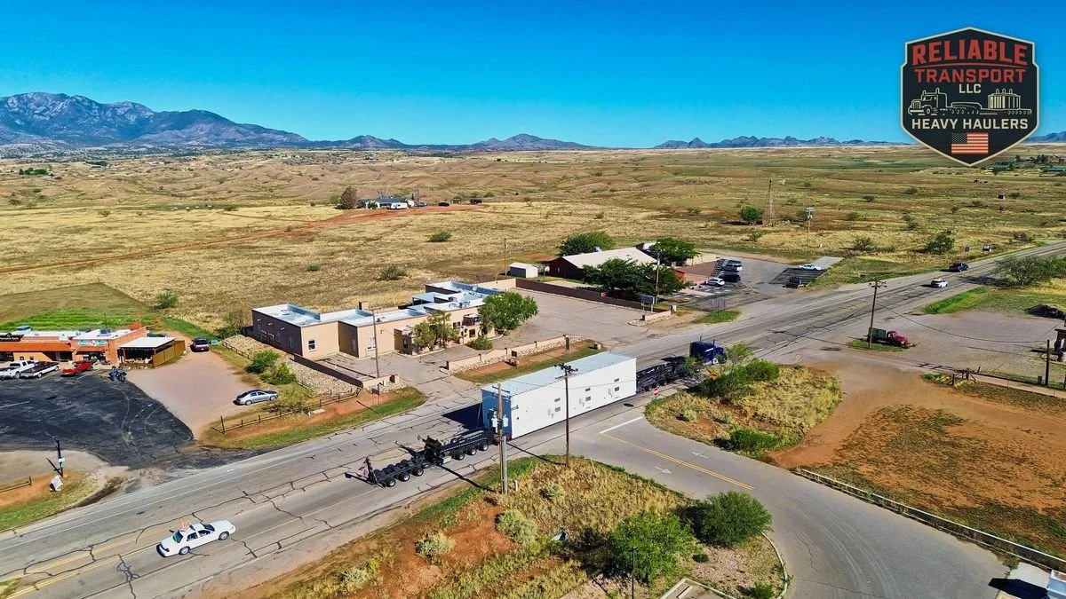 Drone view of a white module on a multi axle trailer passing through a small desert town in Arizona, mountains behind