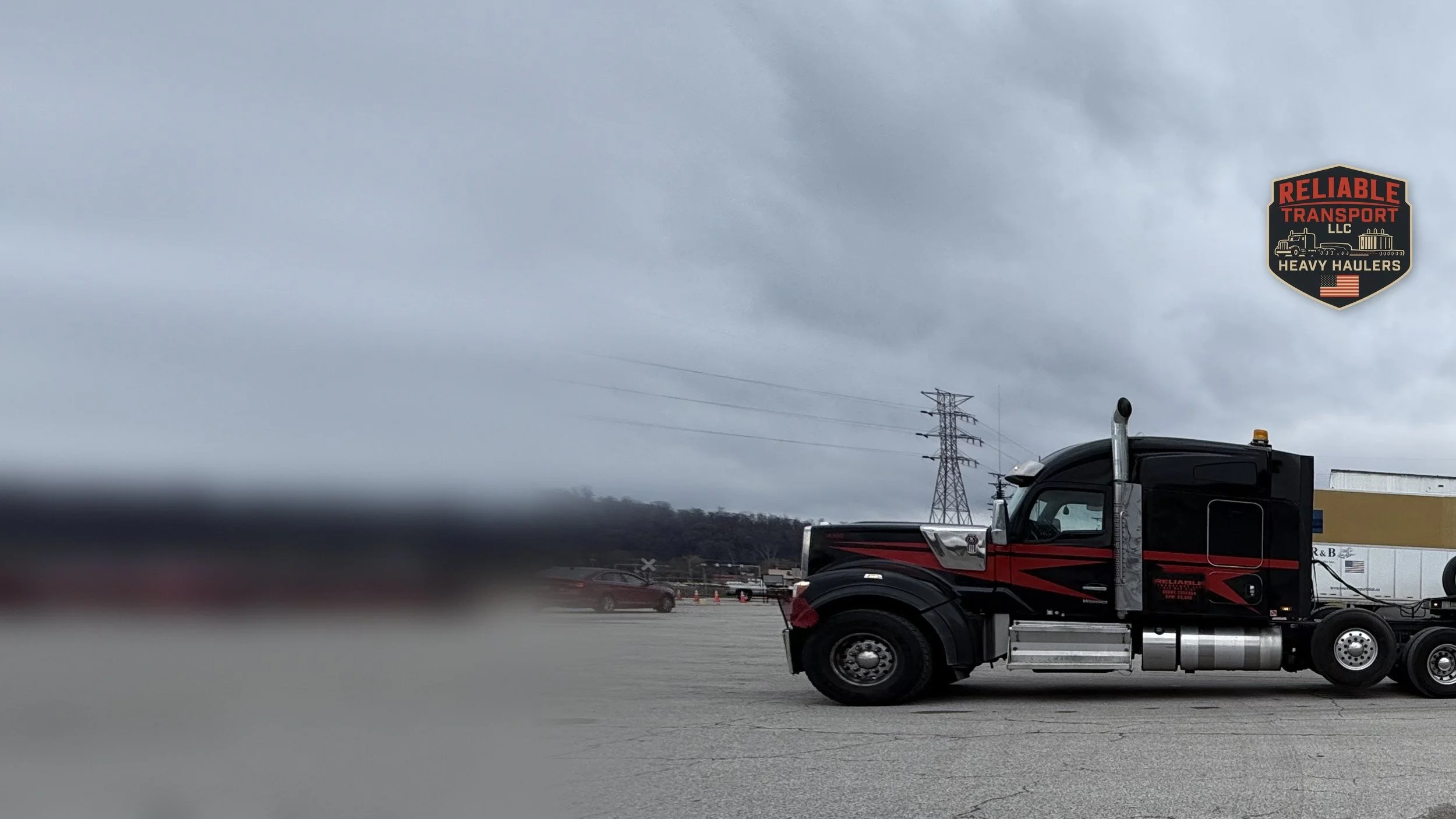 Red and black heavy haul tractor hooked to a multi axle trailer in a large paved lot under a cloudy sky