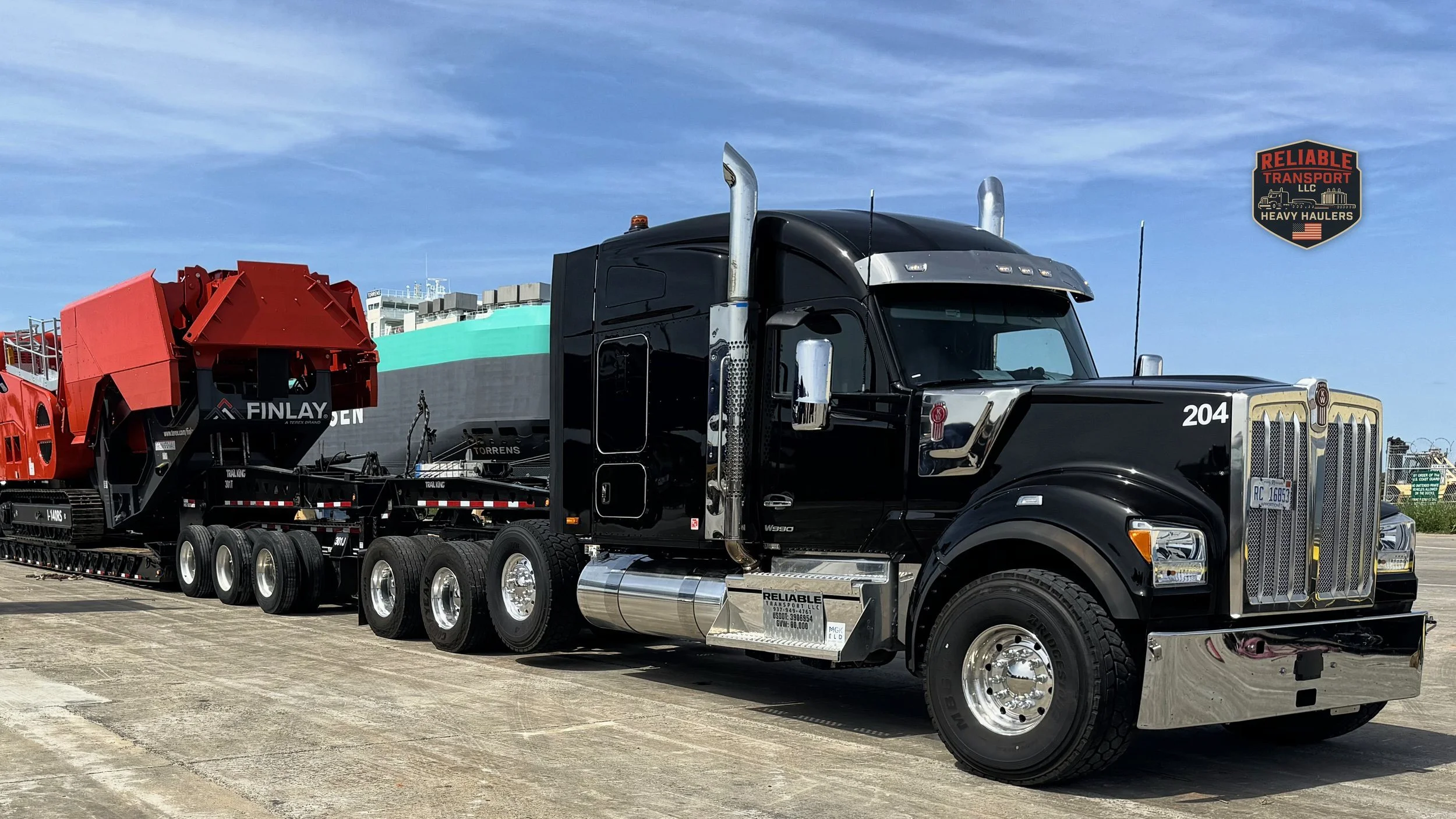 Black heavy haul tractor pulling a red tracked machine on a multi axle trailer across a paved lot