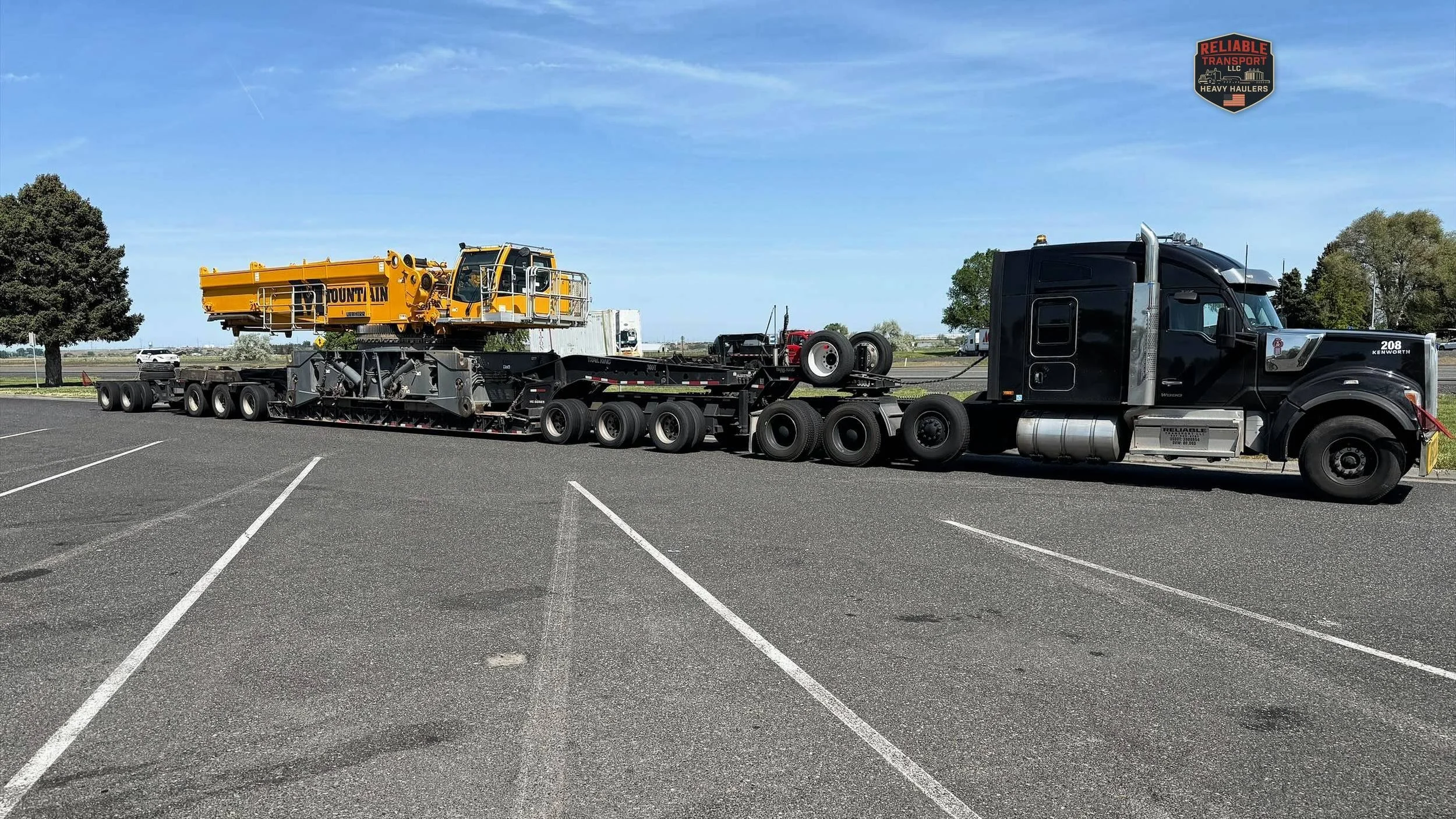 Black heavy haul tractor pulling a yellow crane body on a multi axle trailer across a paved lot