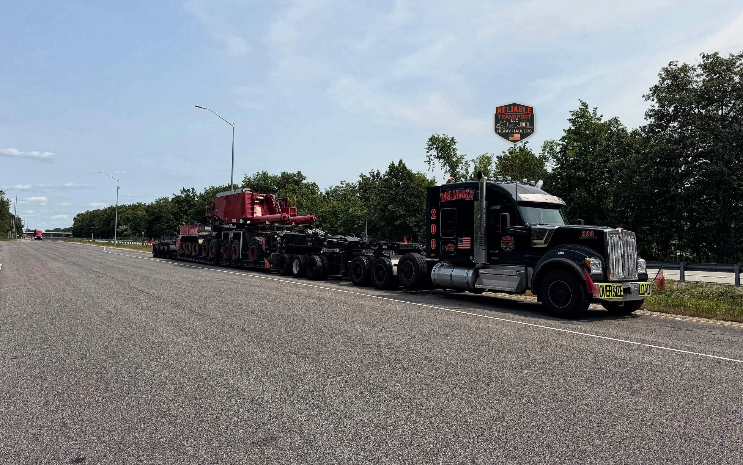Black heavy haul tractor pulling a red crane carrier on a multi axle trailer