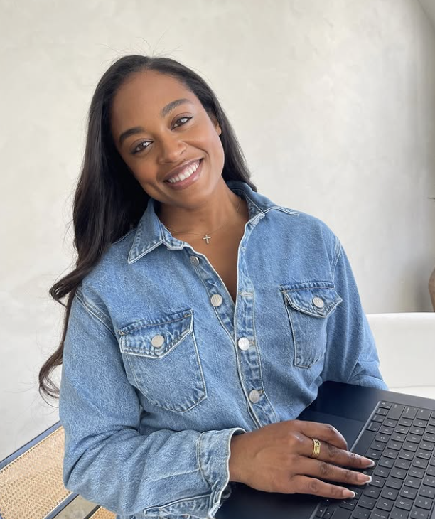 Person in a denim shirt smiling, holding a laptop