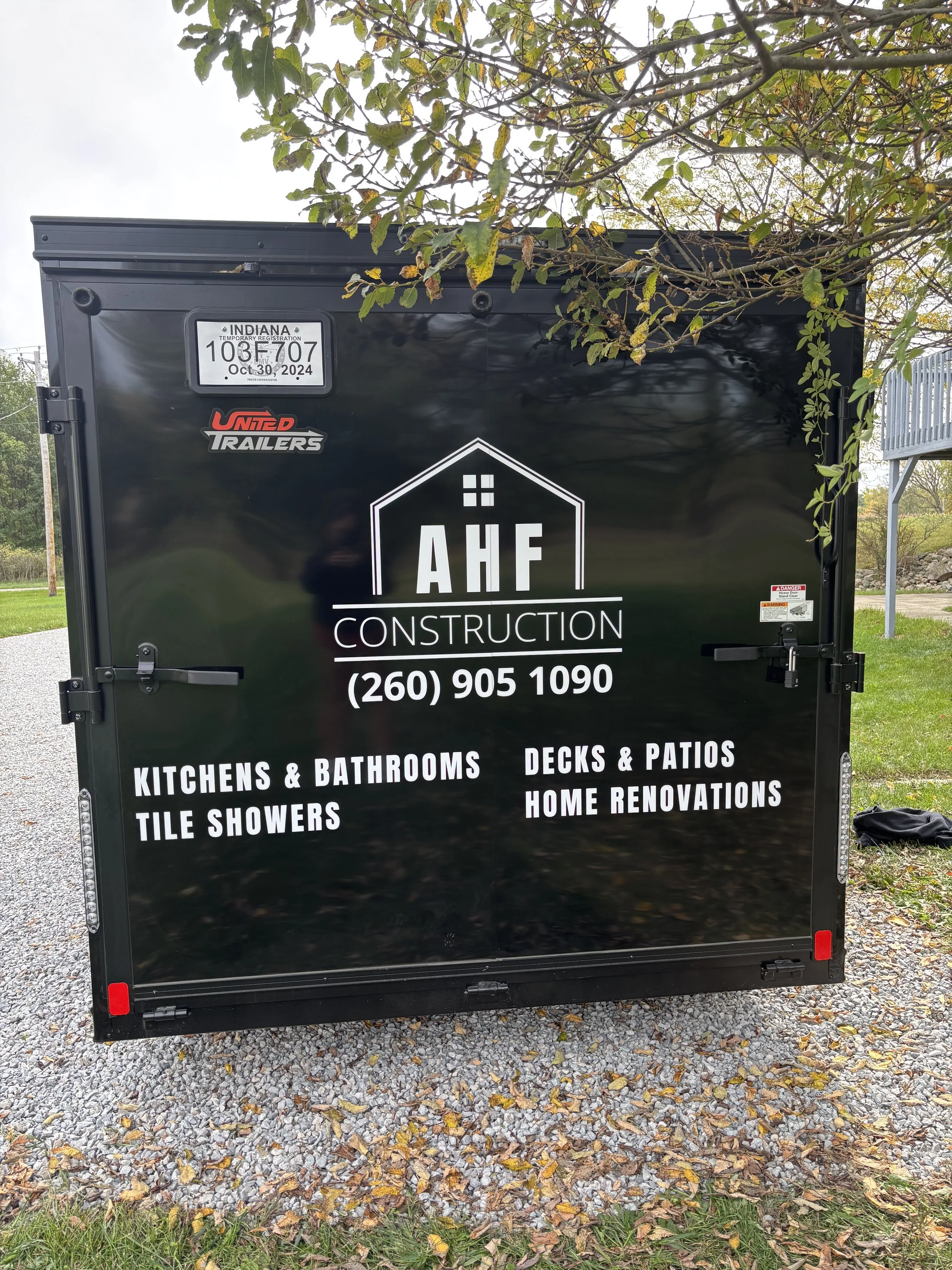 Black construction trailer with white lettering advertising 'AHF Construction,' offering services like kitchens, bathrooms, tile showers, decks, patios, and home renovations. It displays the phone number.