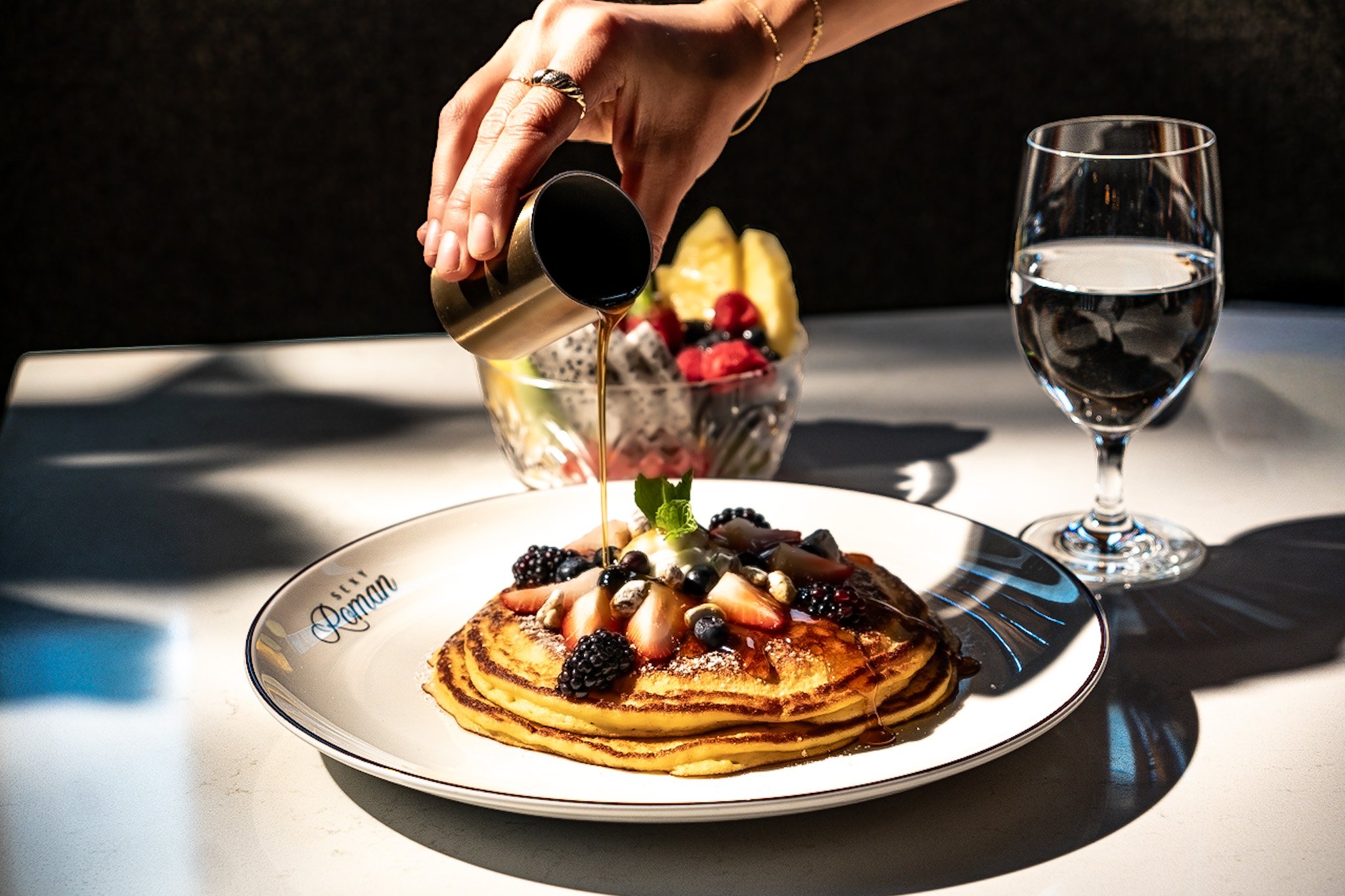 a plate of pancakes with fresh berries and a mother pouring syrup over